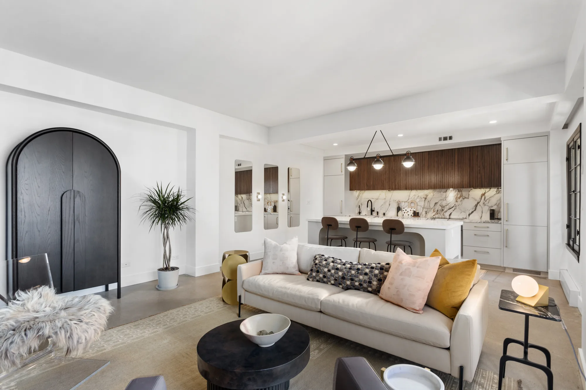 Open-concept living room with a white sofa opening to a kitchen with marble backsplash and a bar-stool island.