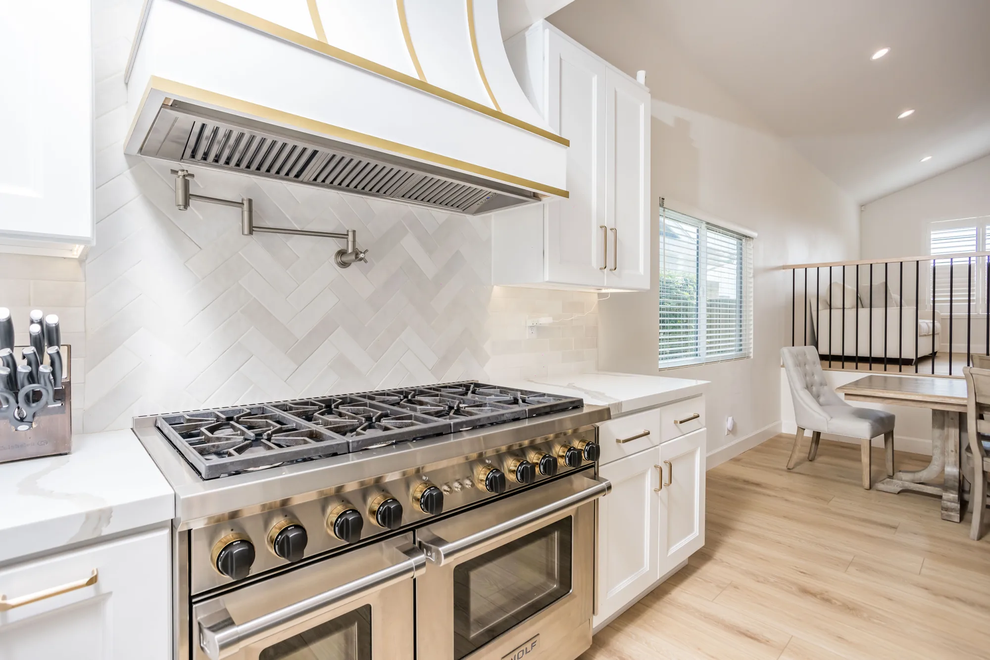 White kitchen with a brass-trimmed hood, professional gas range and herringbone marble backsplash.