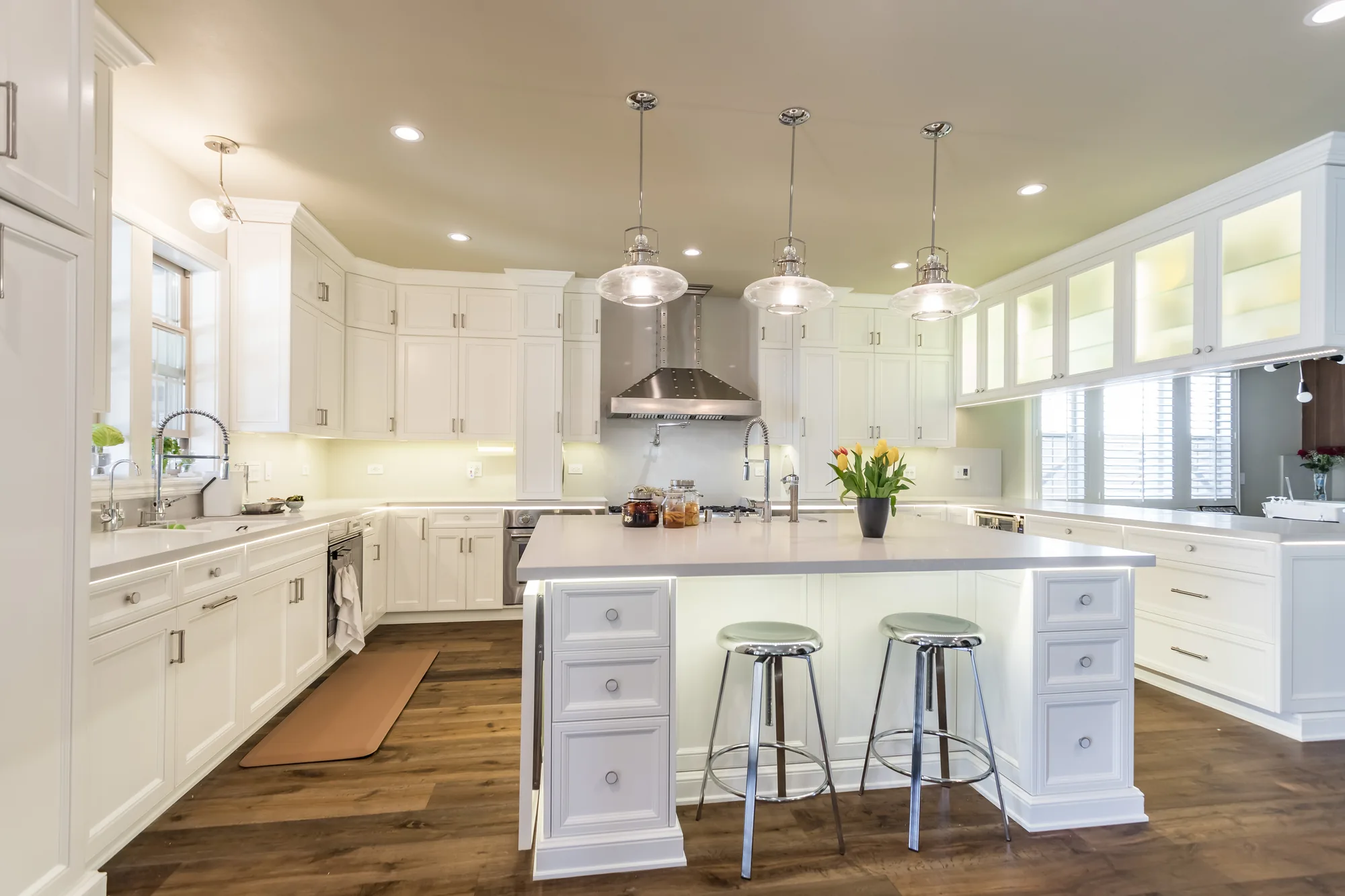 White kitchen with a central island, glass pendant lights and hardwood floors.