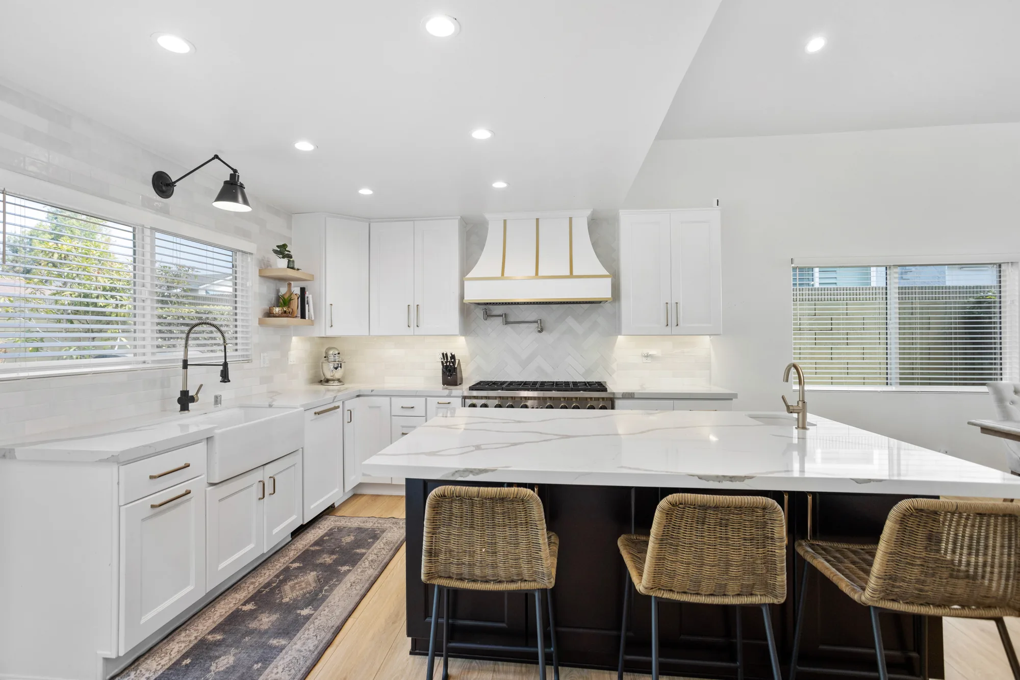 White kitchen with a farmhouse sink, black faucet, herringbone backsplash and a dark island topped with white marble.
