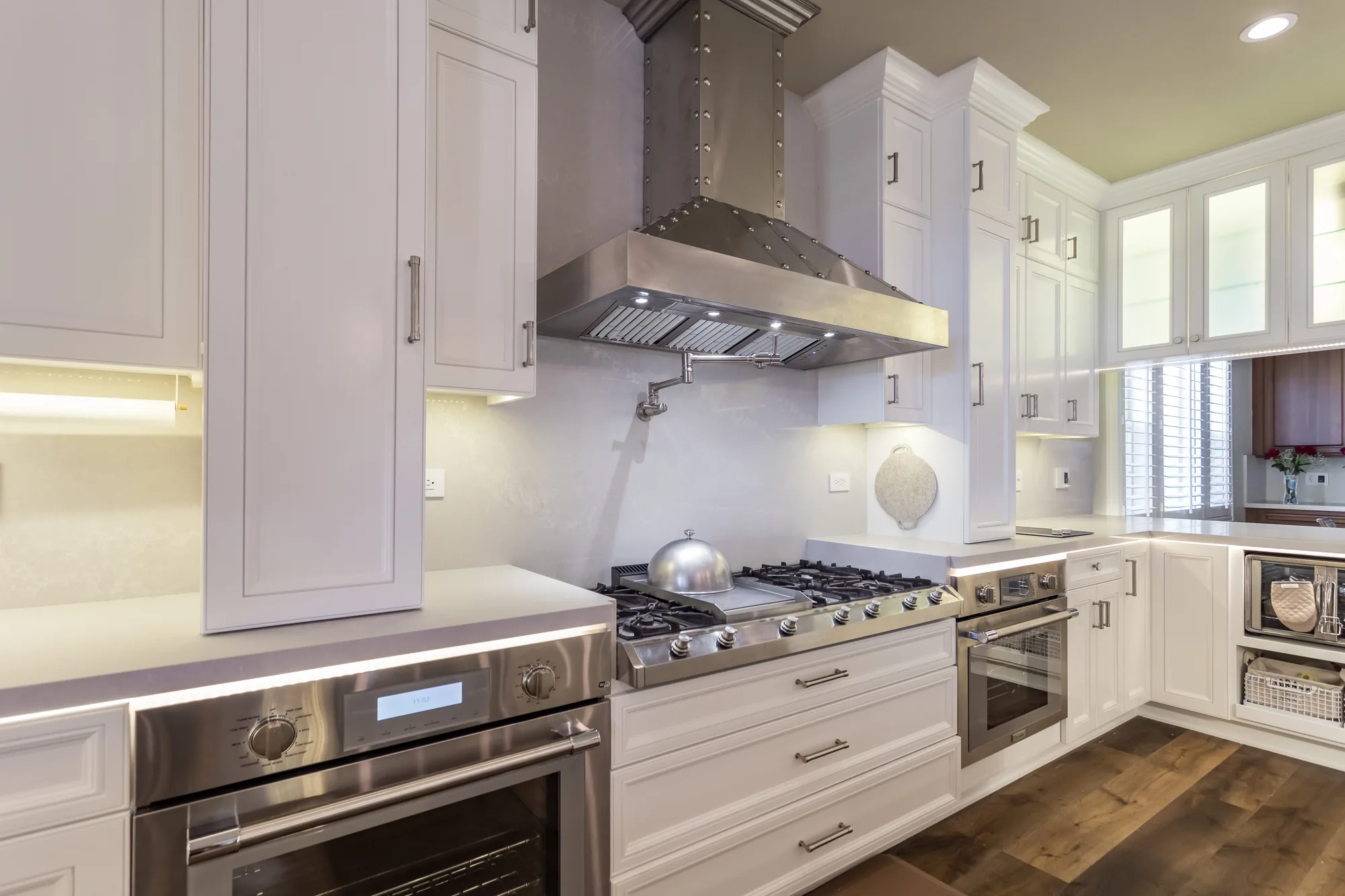 White kitchen with a riveted steel range hood, gas cooktop and glass-front upper cabinets.