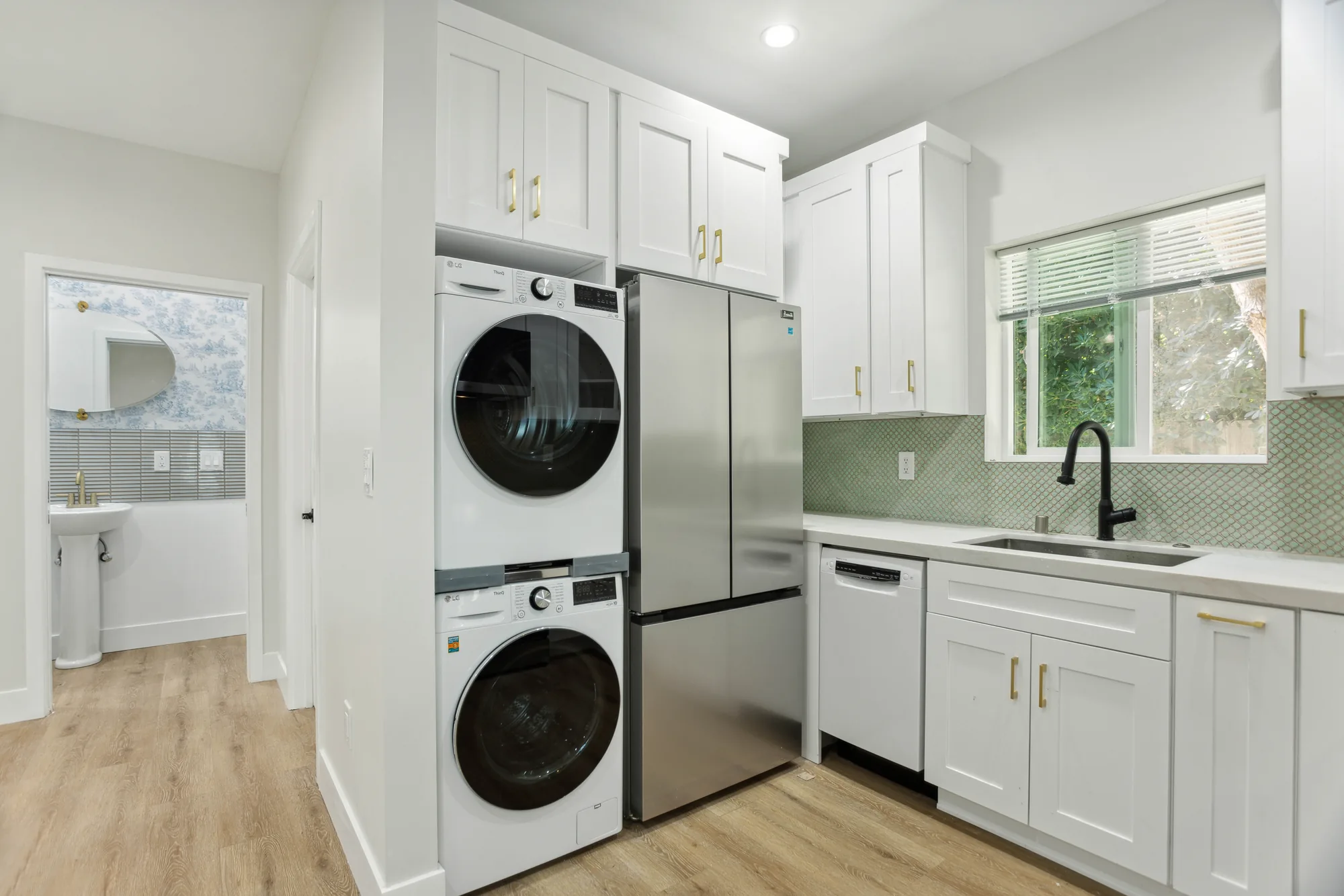 Kitchen wall with stacked laundry, stainless refrigerator and white cabinets with brass pulls.