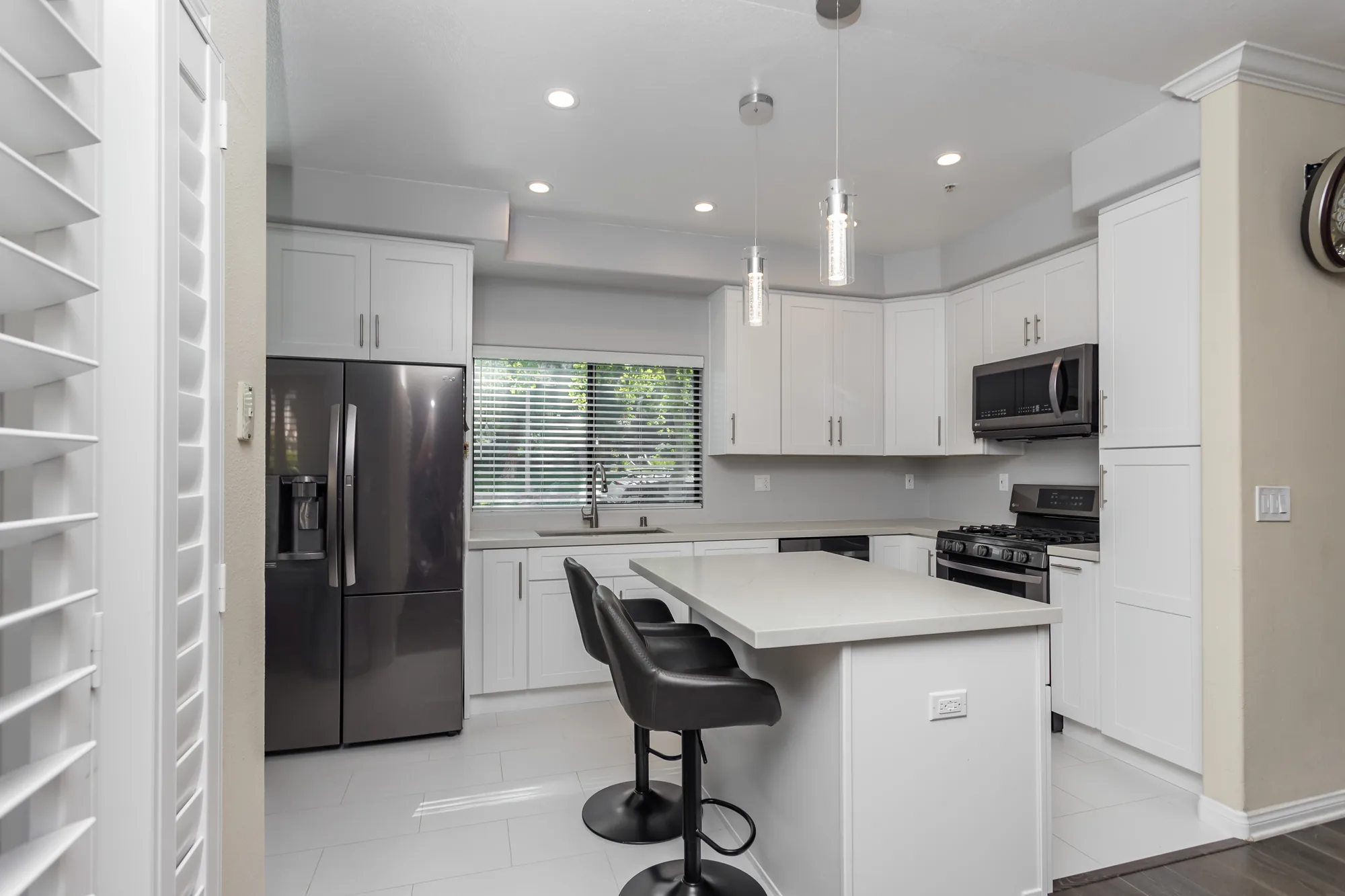 Finished kitchen seen through a doorway with a french-door refrigerator, island, and pendant lights.