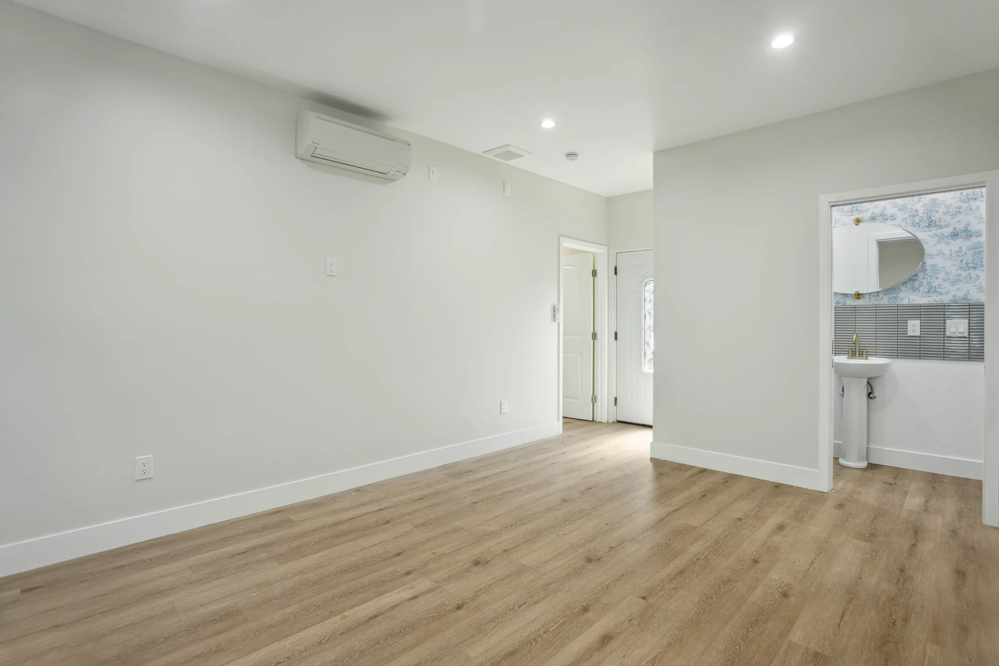 Empty living room with a wall-mounted mini-split head, plank flooring and a door to the outside.