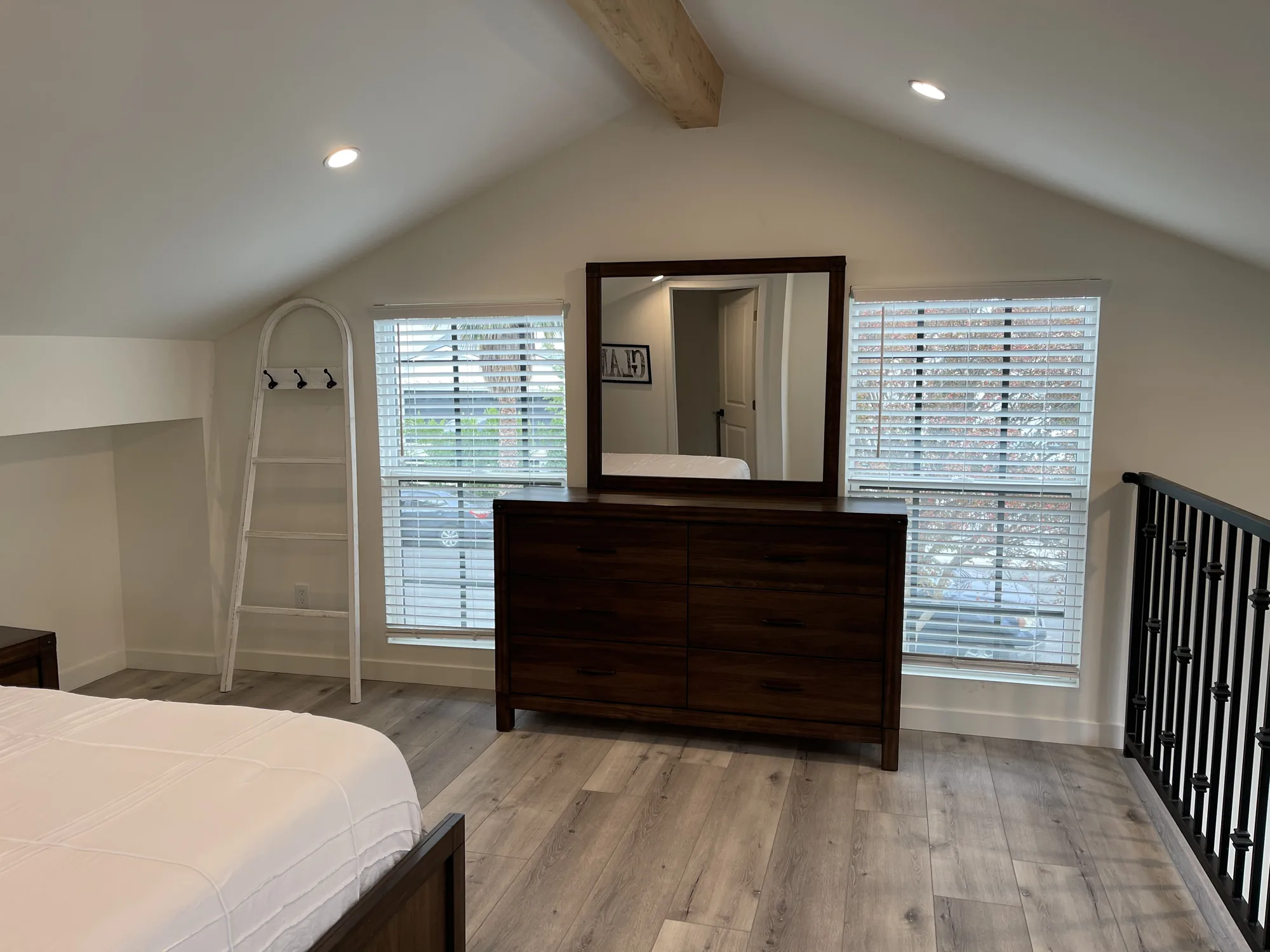 Loft bedroom wall with a dresser and mirror between two blinded windows under a vaulted ceiling.