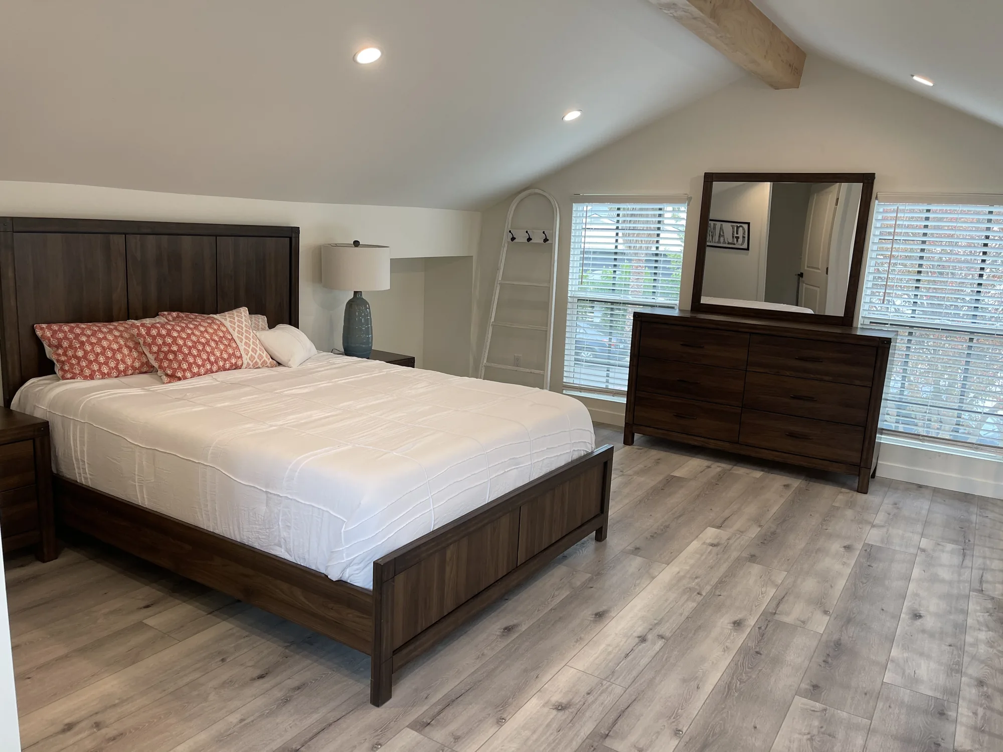 Loft bedroom with a vaulted ceiling, wood beam, dark wood bed and dresser, and plank flooring.