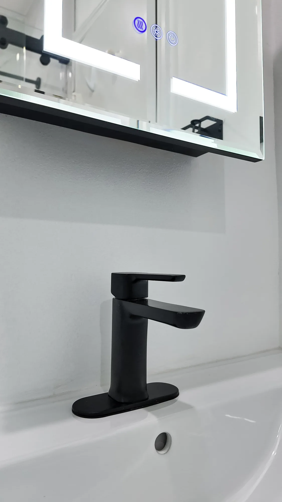 Close-up of a matte black single-handle faucet on a white ceramic sink under a lighted mirror.