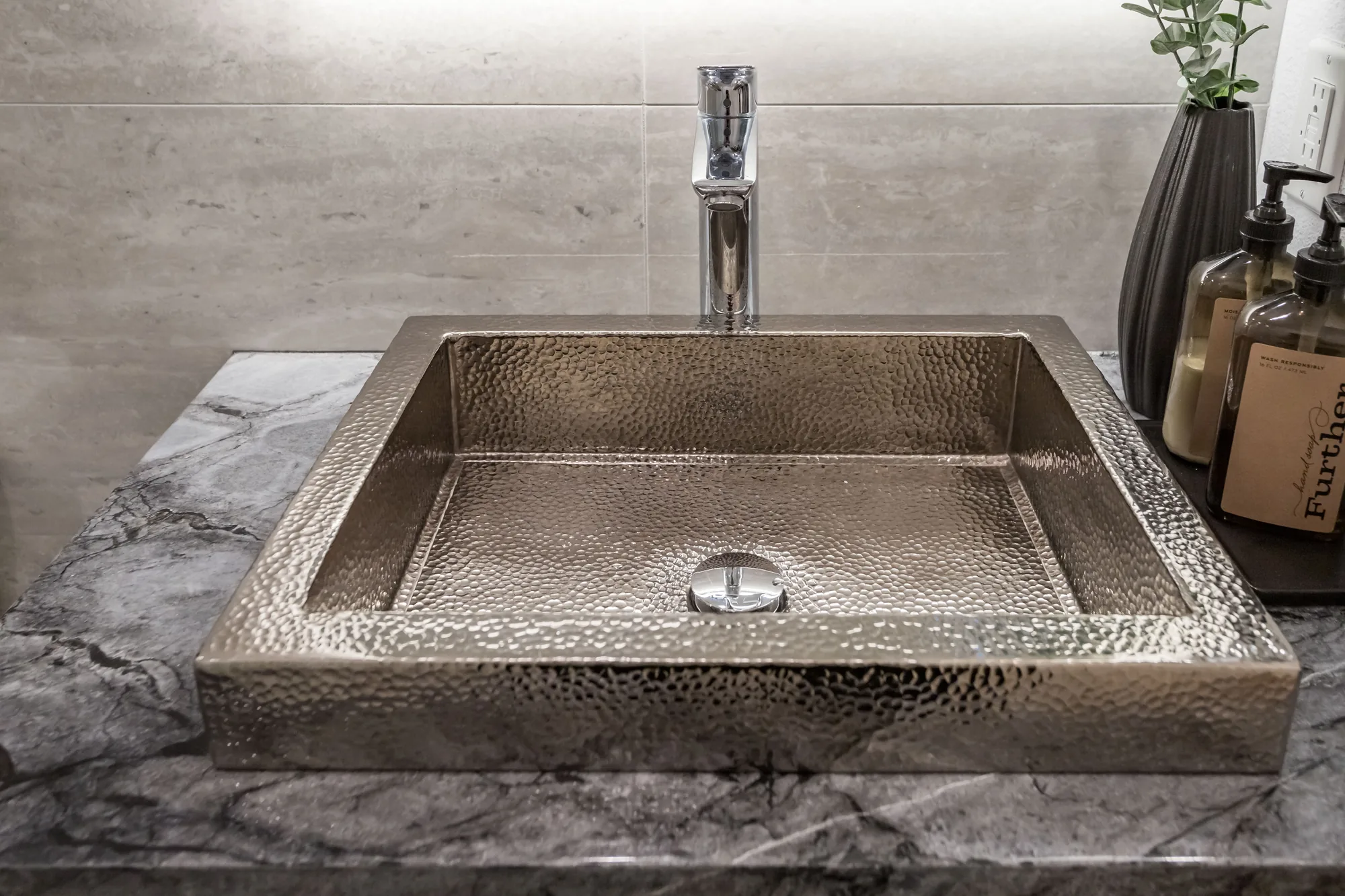 Hammered nickel-tone sink basin on a marble-look vanity top with a chrome single-handle faucet.