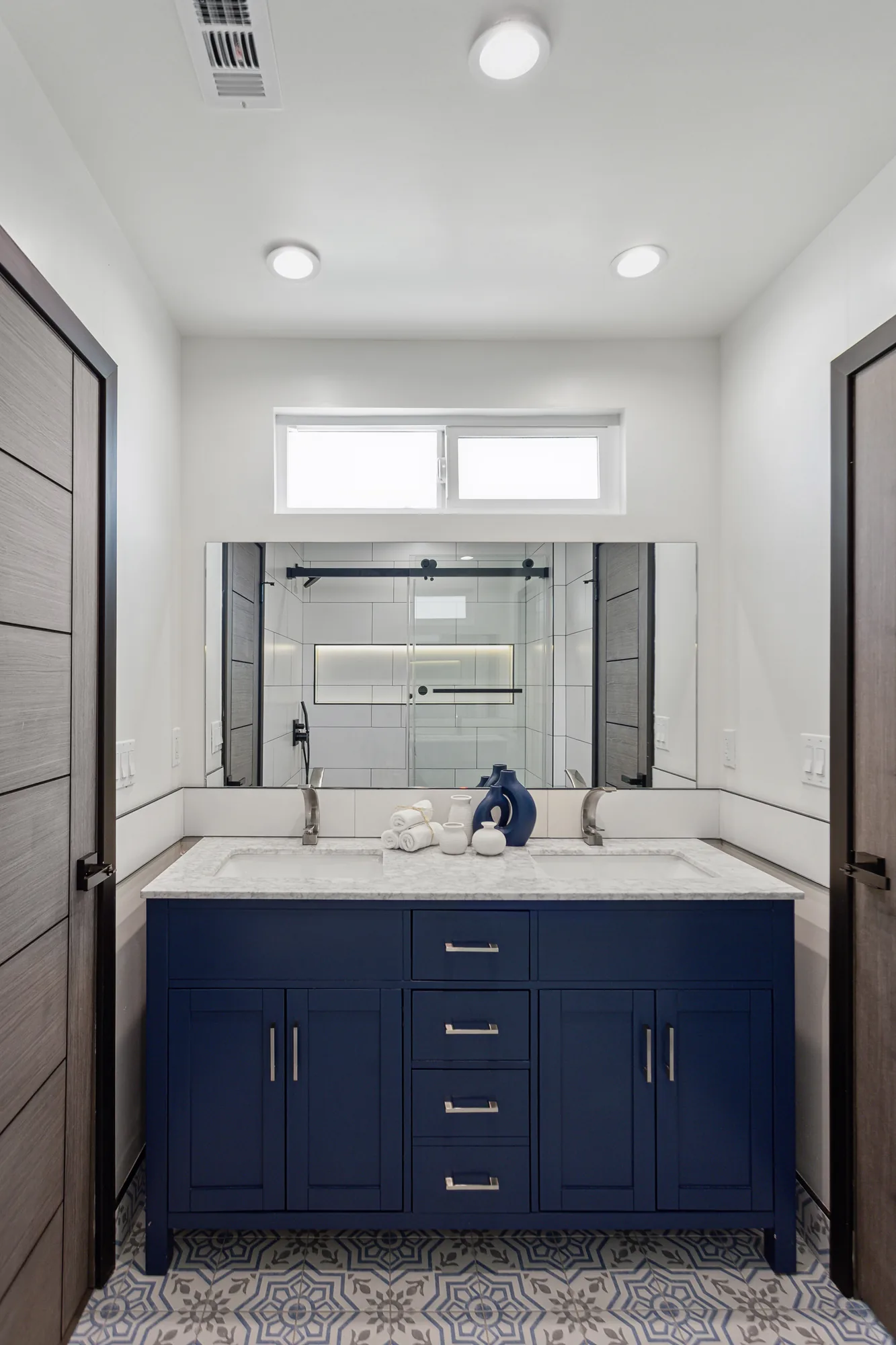 Navy double vanity with marble-look counter, large mirror and patterned tile floor in a bathroom.