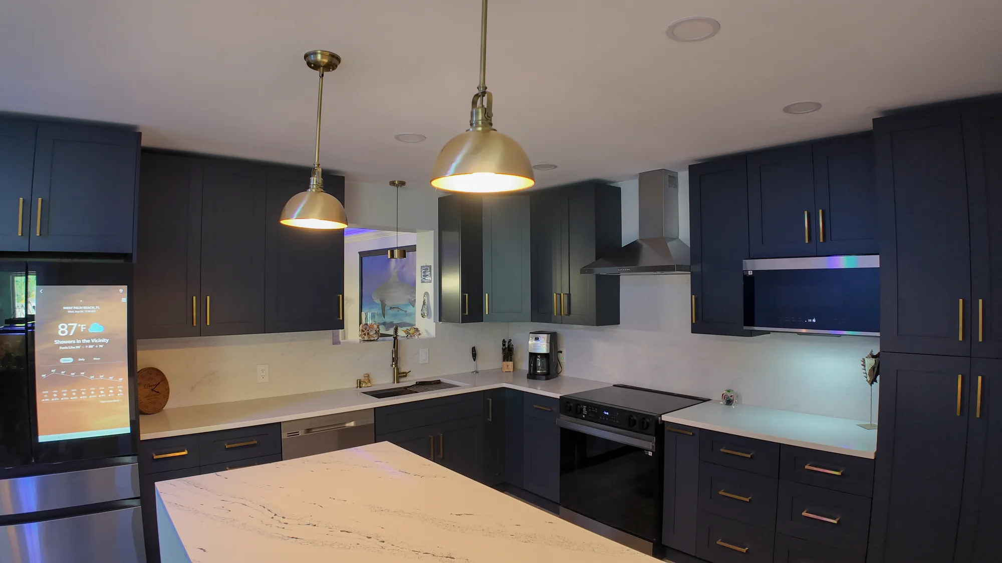 Navy kitchen glowing under brass pendants and LED strips, with quartz counters and a stainless range.