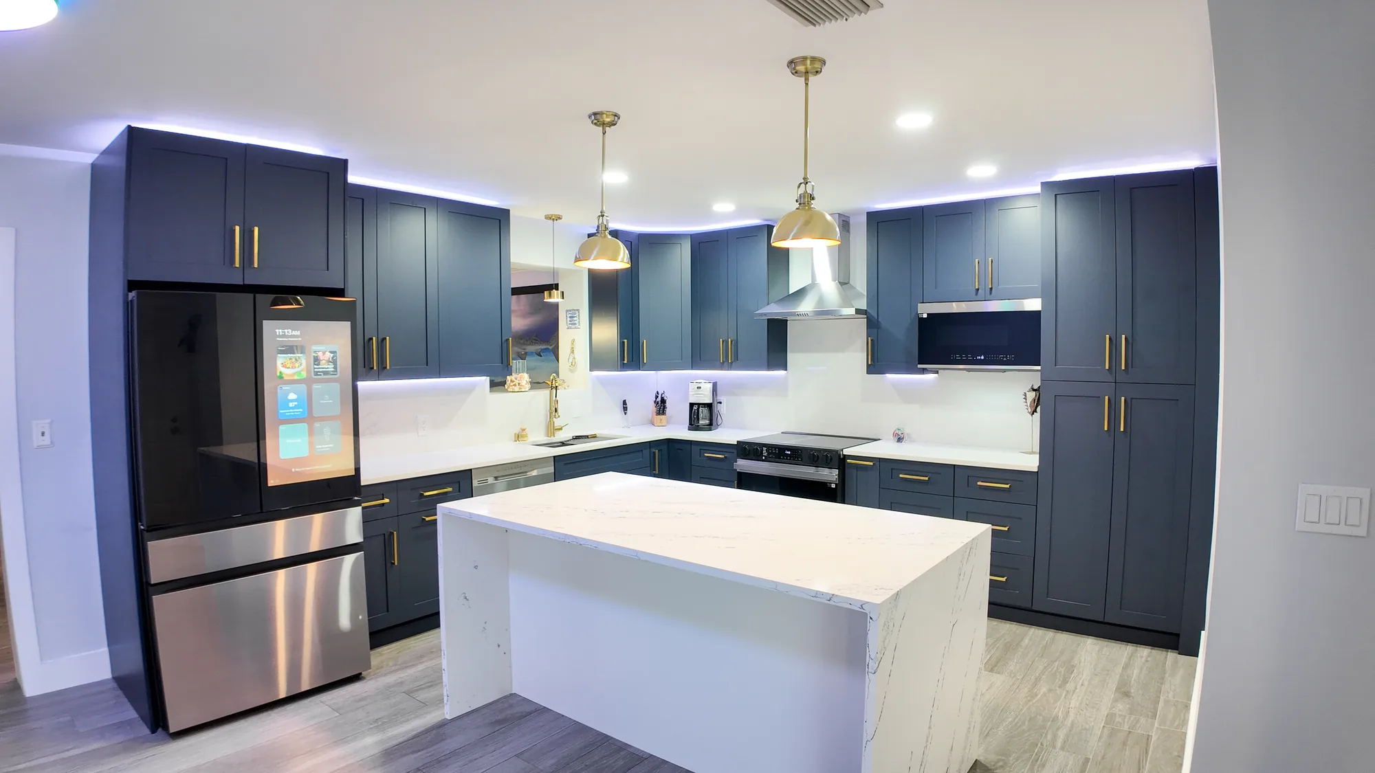 Remodeled kitchen with navy blue shaker cabinets, brass hardware and a white quartz waterfall island.