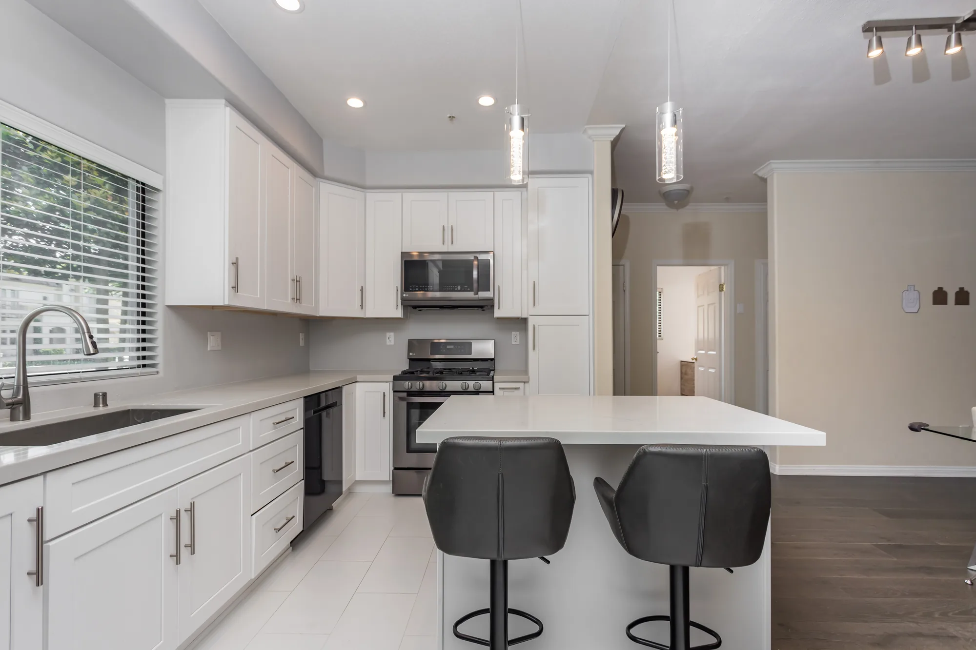 Wide view of a finished white kitchen with a seated island, two glass pendants, and gray bar stools.