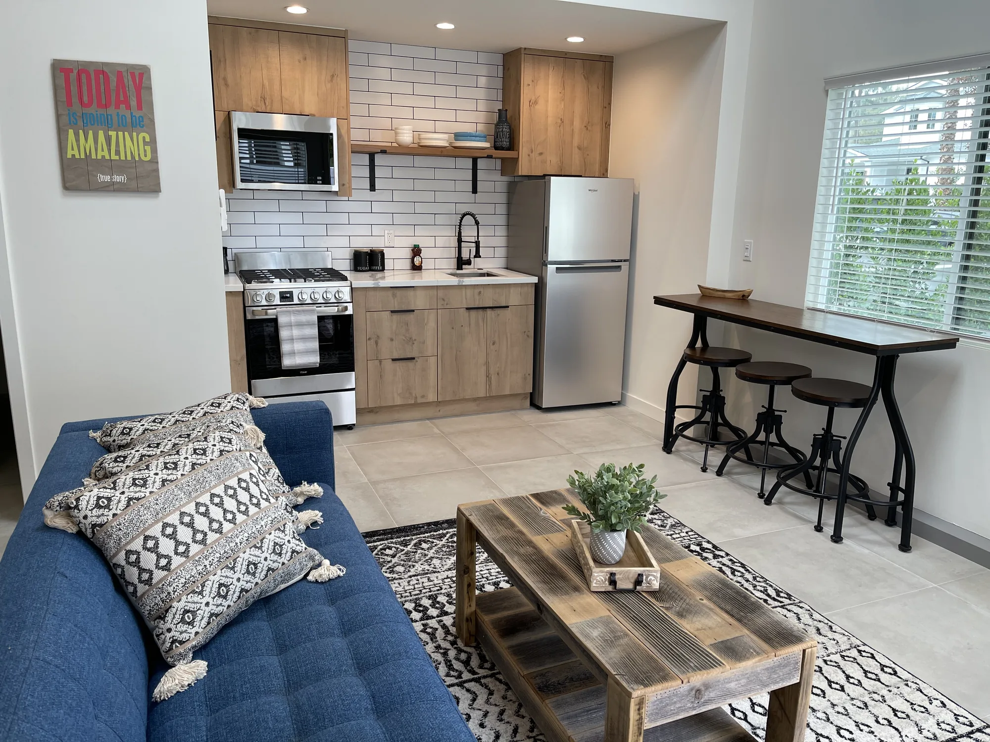 Open kitchen with oak-look cabinets and subway tile beside a living area and counter-height table.