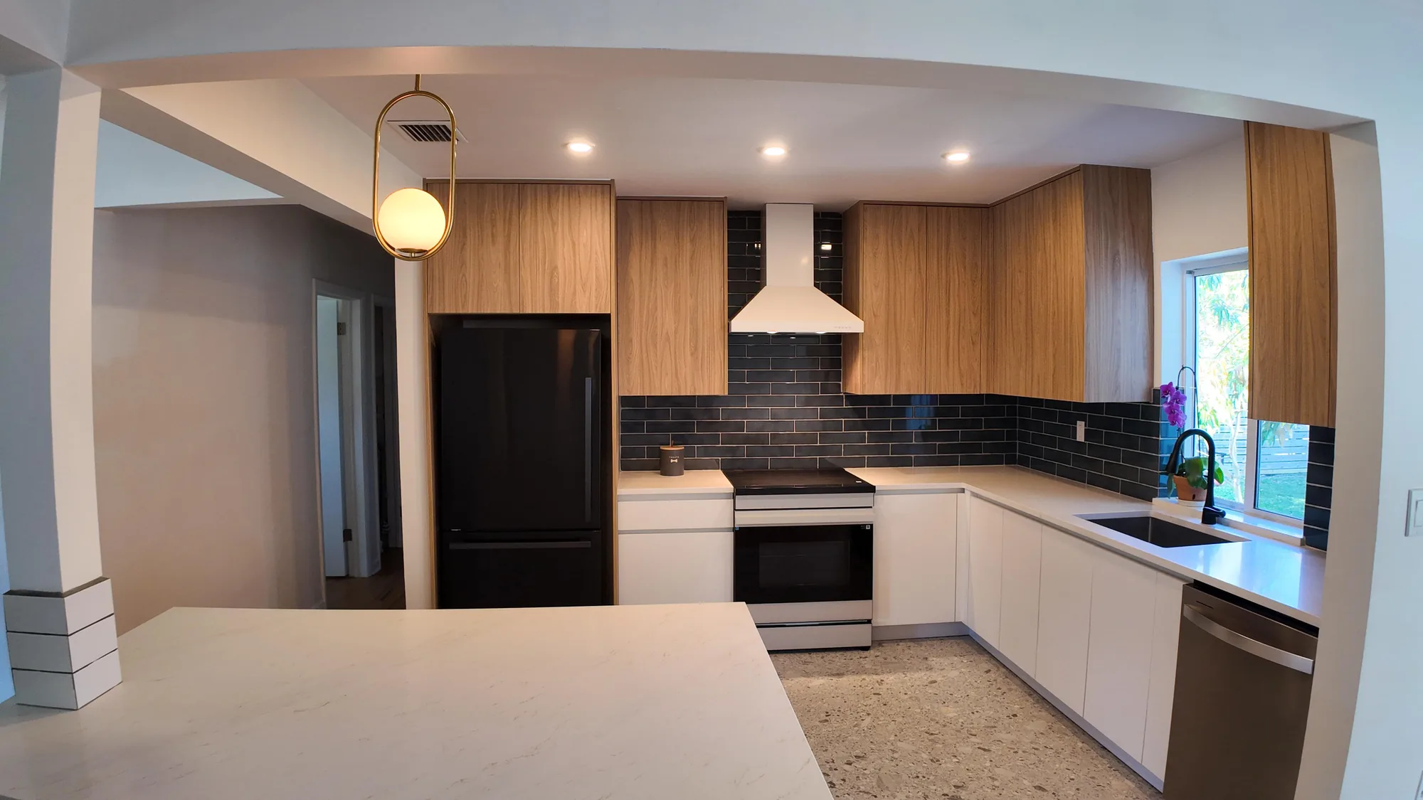 Open kitchen seen past a quartz peninsula, with a brass globe pendant and dark tile backsplash beyond.
