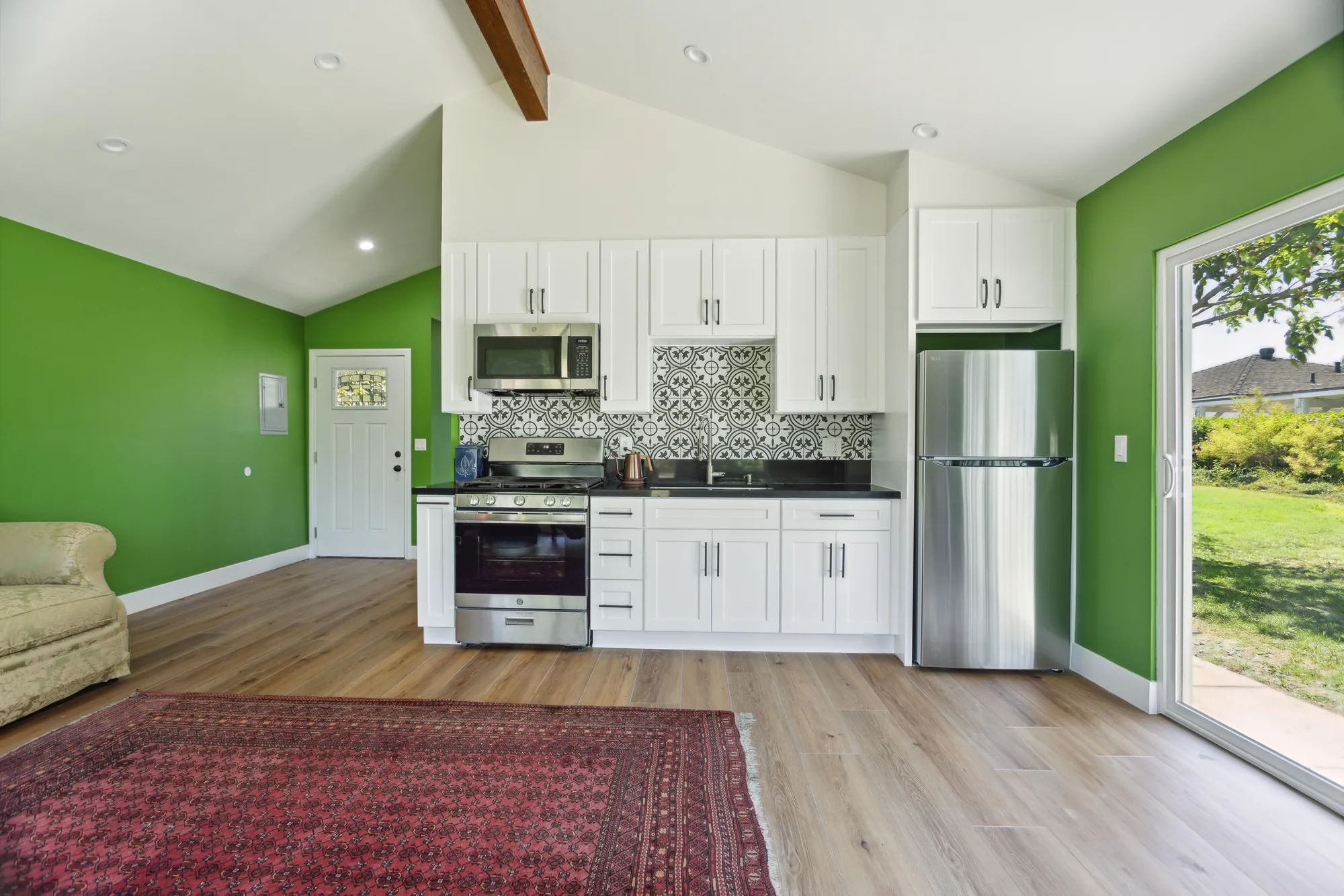 Open living area with vaulted ceiling and a white shaker kitchen along a bright green wall.