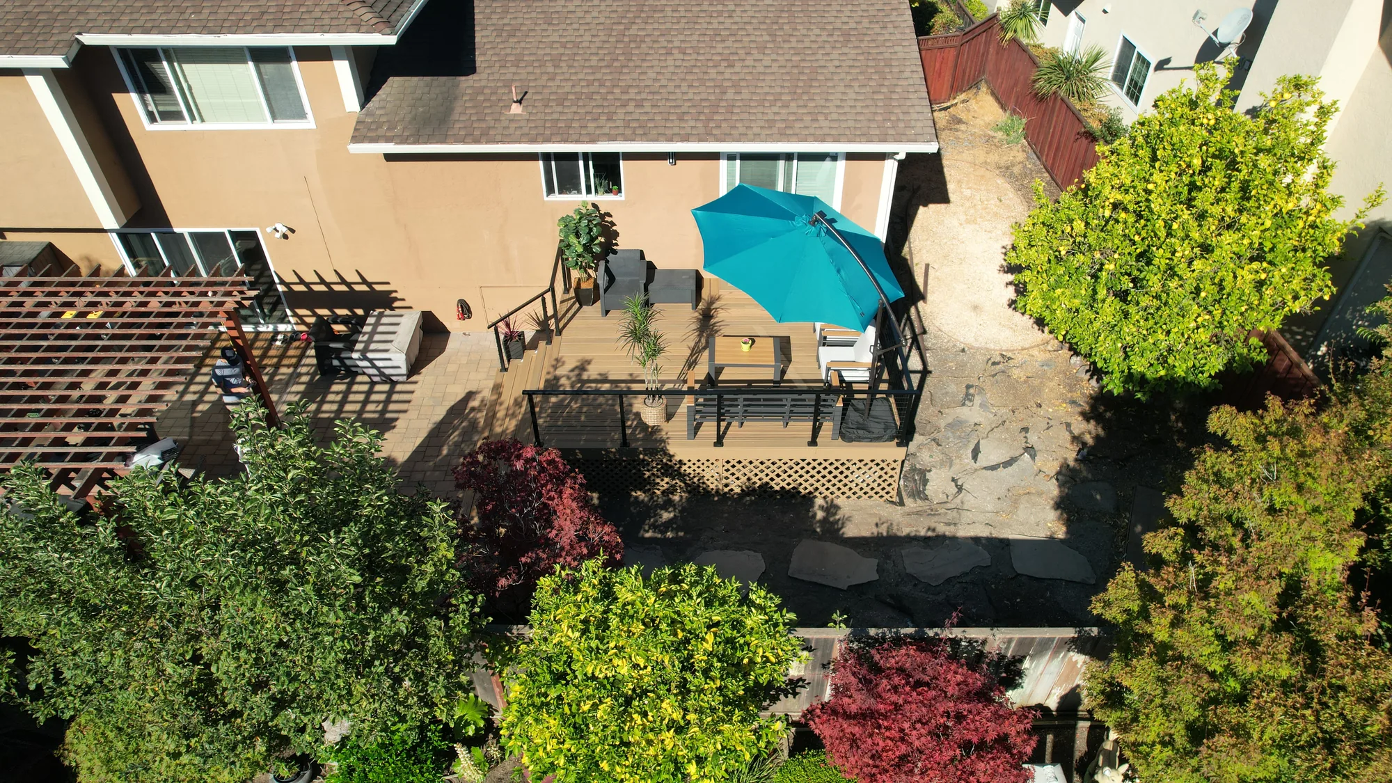Overhead drone view of a finished backyard deck with umbrella, patio seating and landscaped garden beds.