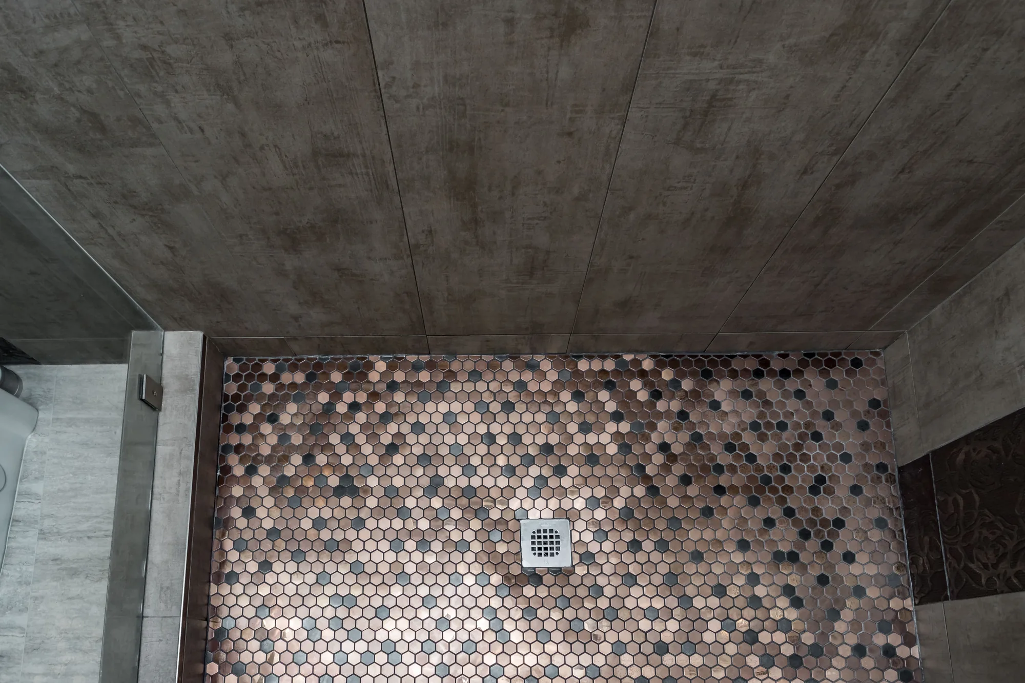 Overhead view of the shower floor showing hex mosaic tile and a square brushed drain.
