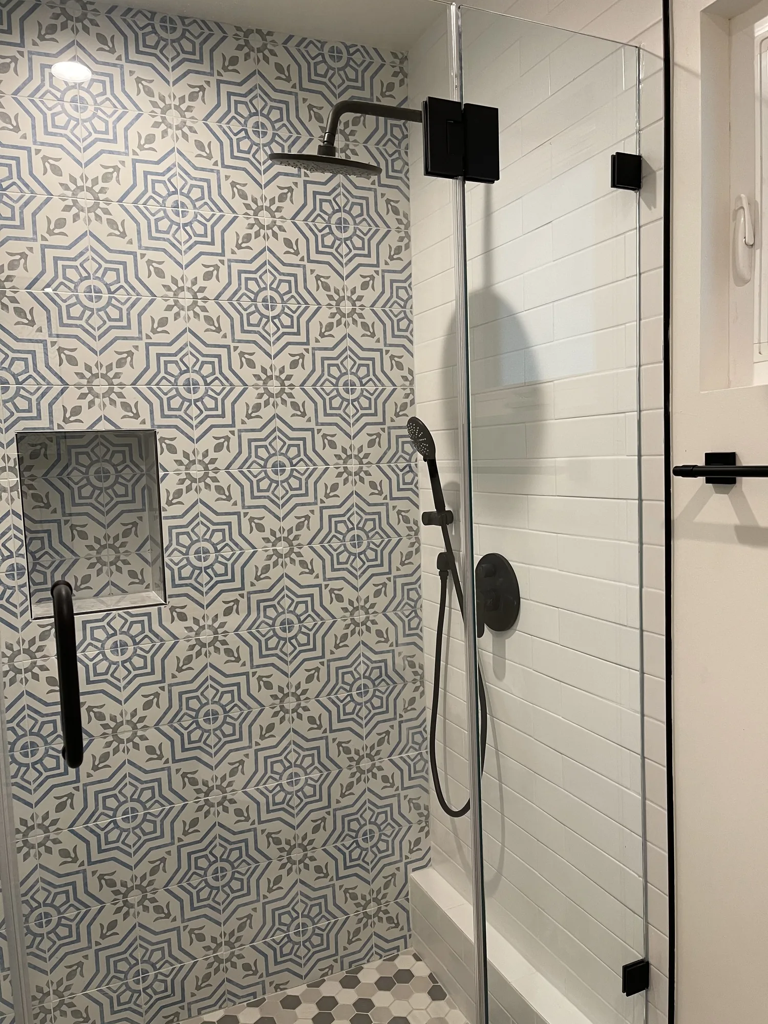 Shower with a patterned blue and white tile wall, recessed niche and matte black rain fixtures.