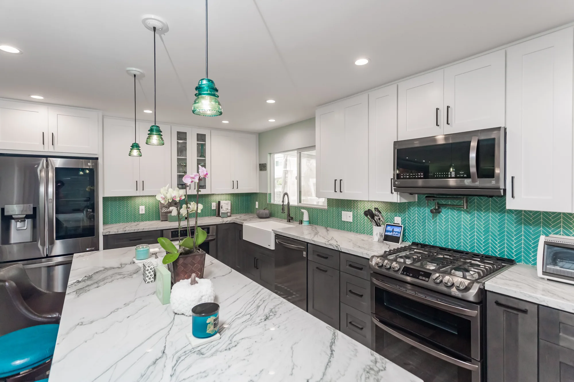 Three glass pendant lights hang over a veined stone island facing the sink and range wall.