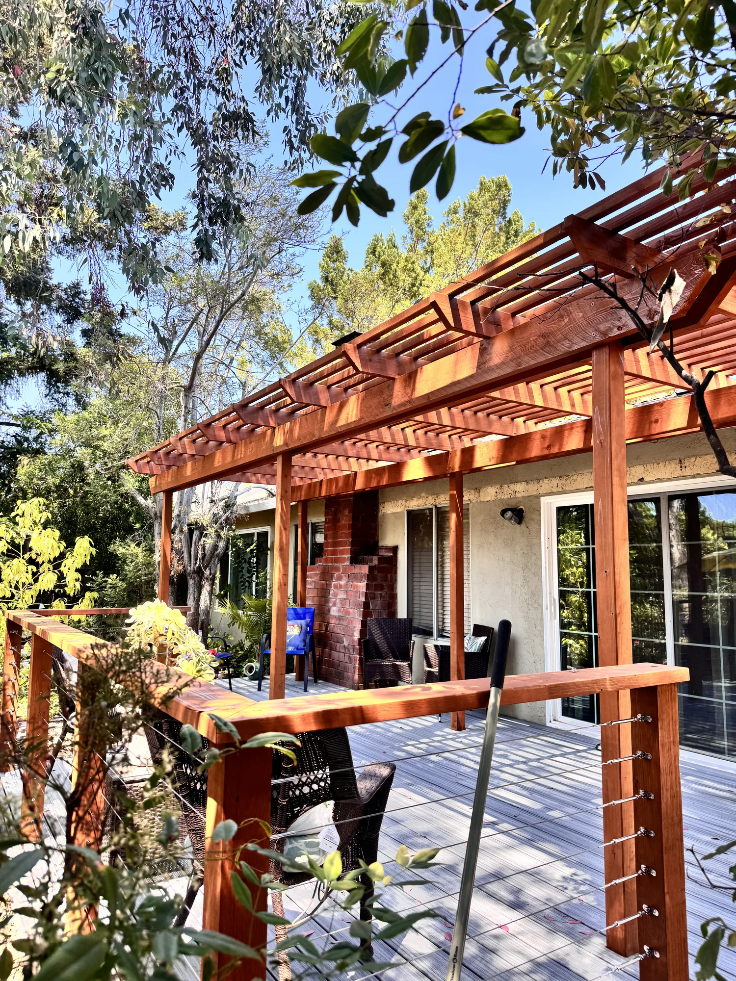Stained wood pergola beams overhead with a cable railing and wood cap rail along the deck edge.