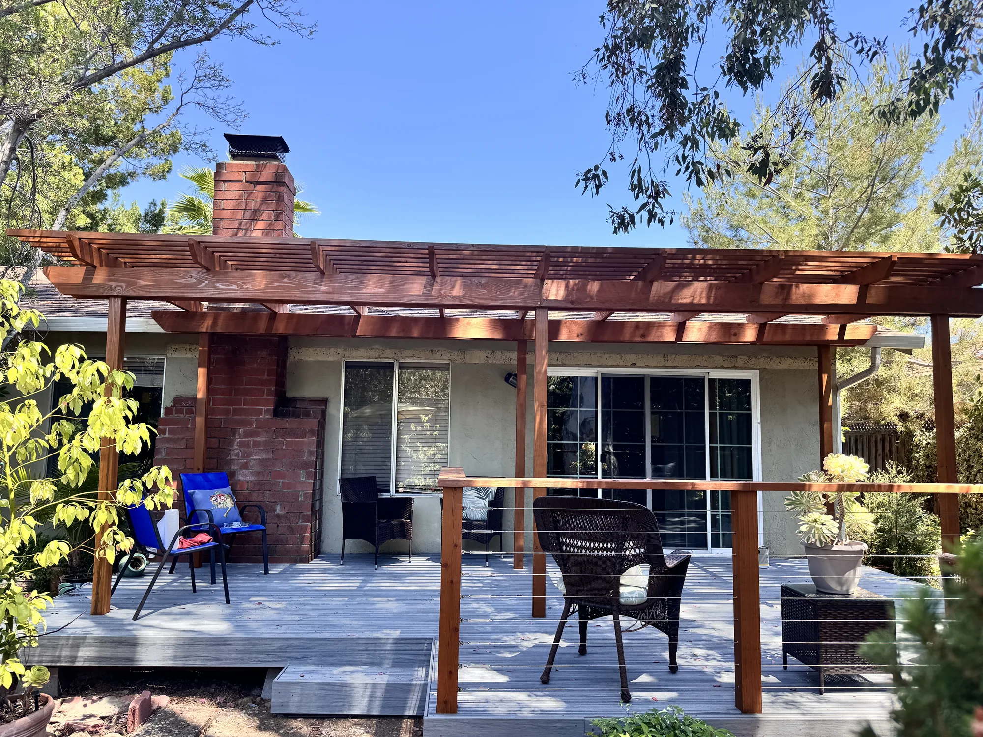 Front-facing view of a stained wood pergola spanning a gray deck with cable railing and patio doors.