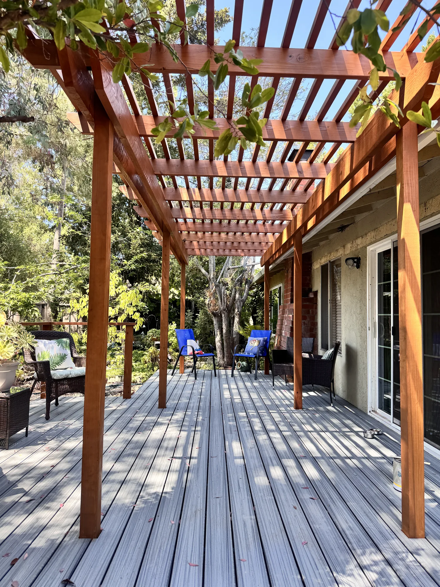 Long gray deck running beside a stucco house under a stained wood pergola with slatted rafters.