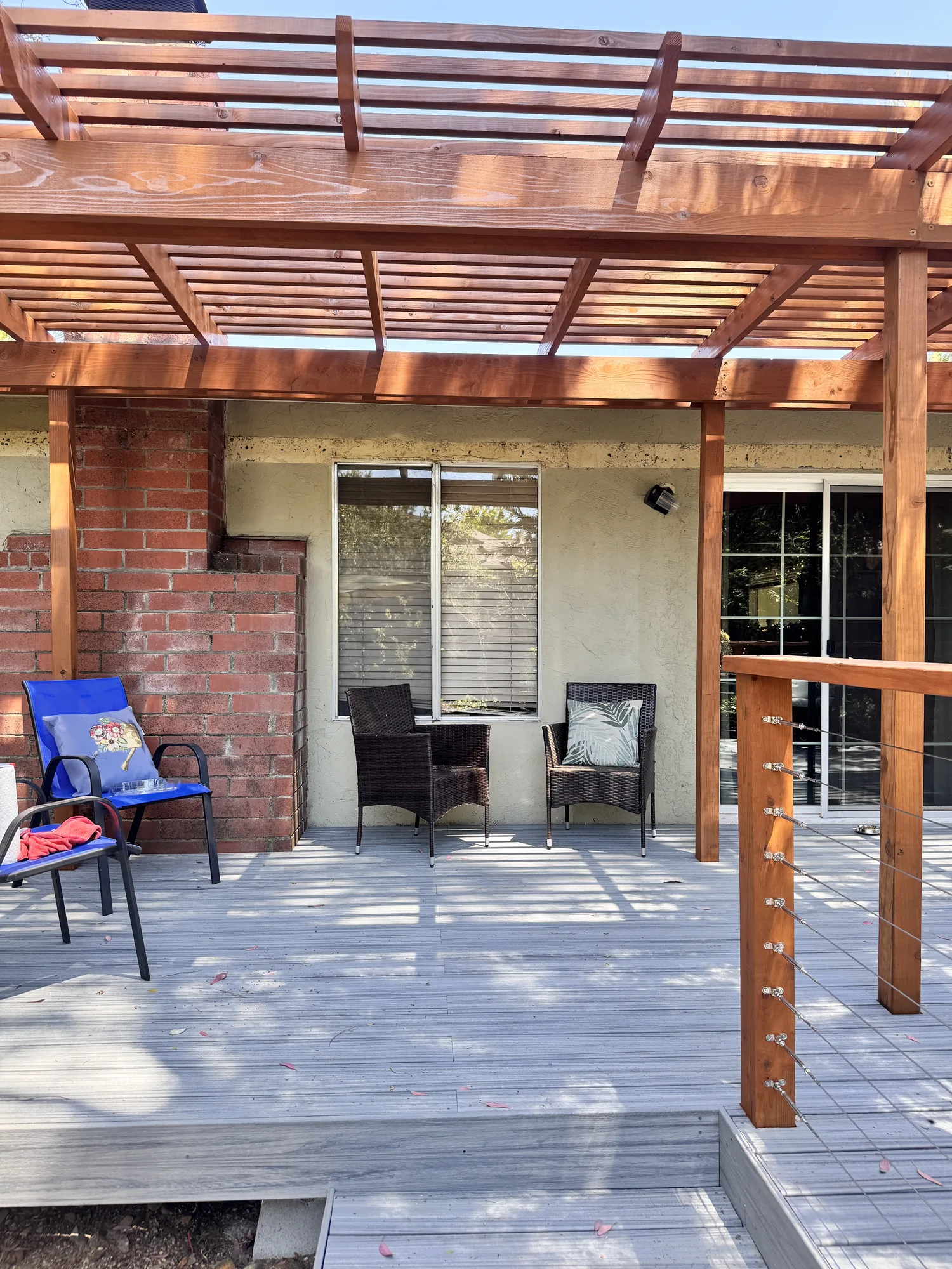 Looking up at closely spaced pergola rafters shading a deck seating area against a stucco wall.