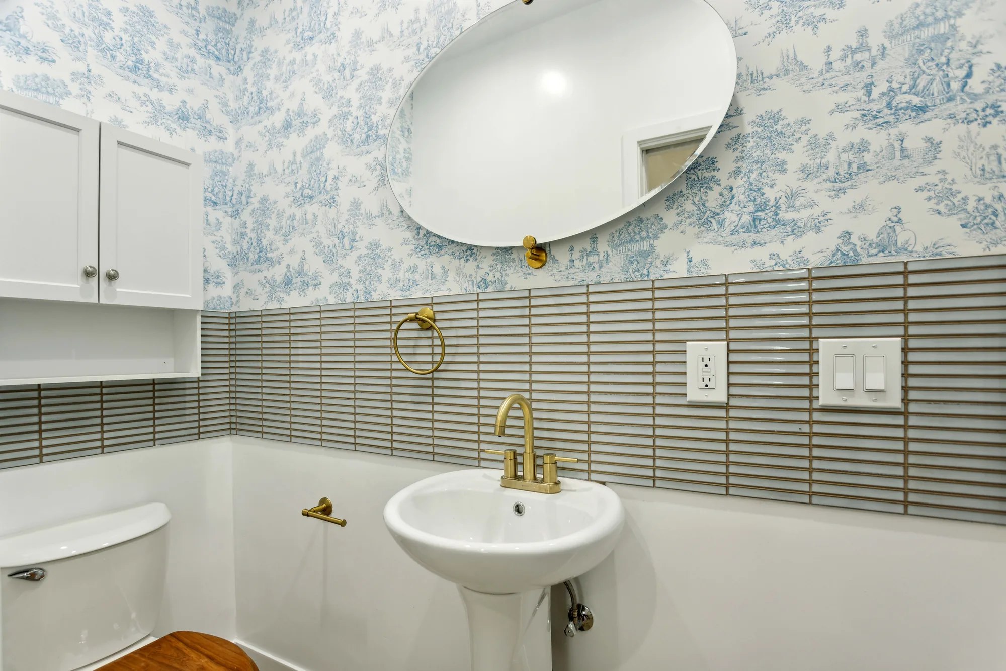 Powder room with blue patterned wallpaper, linear tile wainscot and a white pedestal sink.