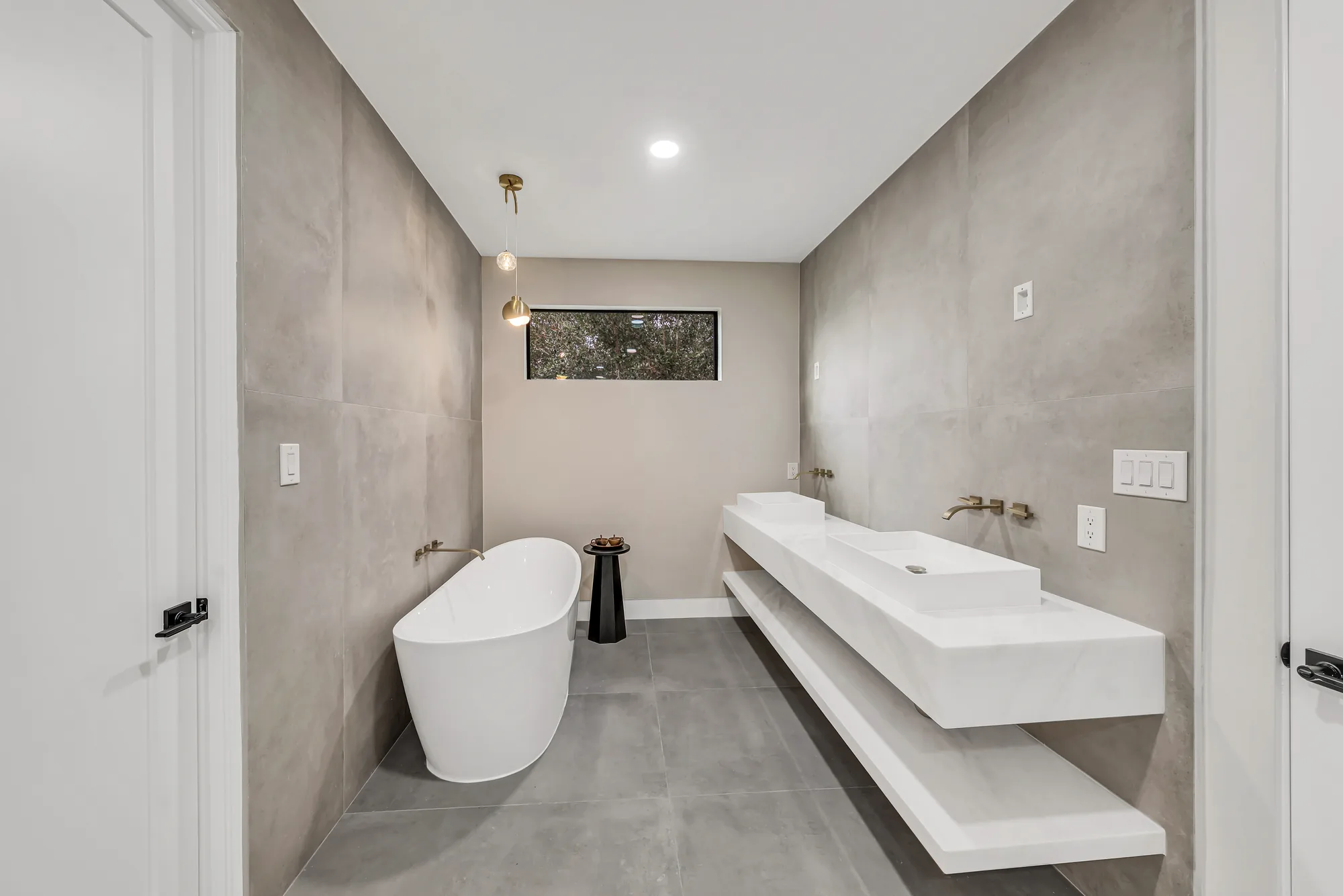 Wide primary bathroom with freestanding tub, floating stone double vanity and gray concrete-look tile walls.
