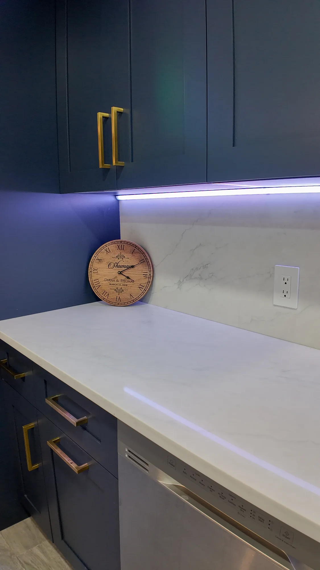Detail of navy upper cabinets, an LED light strip and a white quartz counter with matching backsplash.