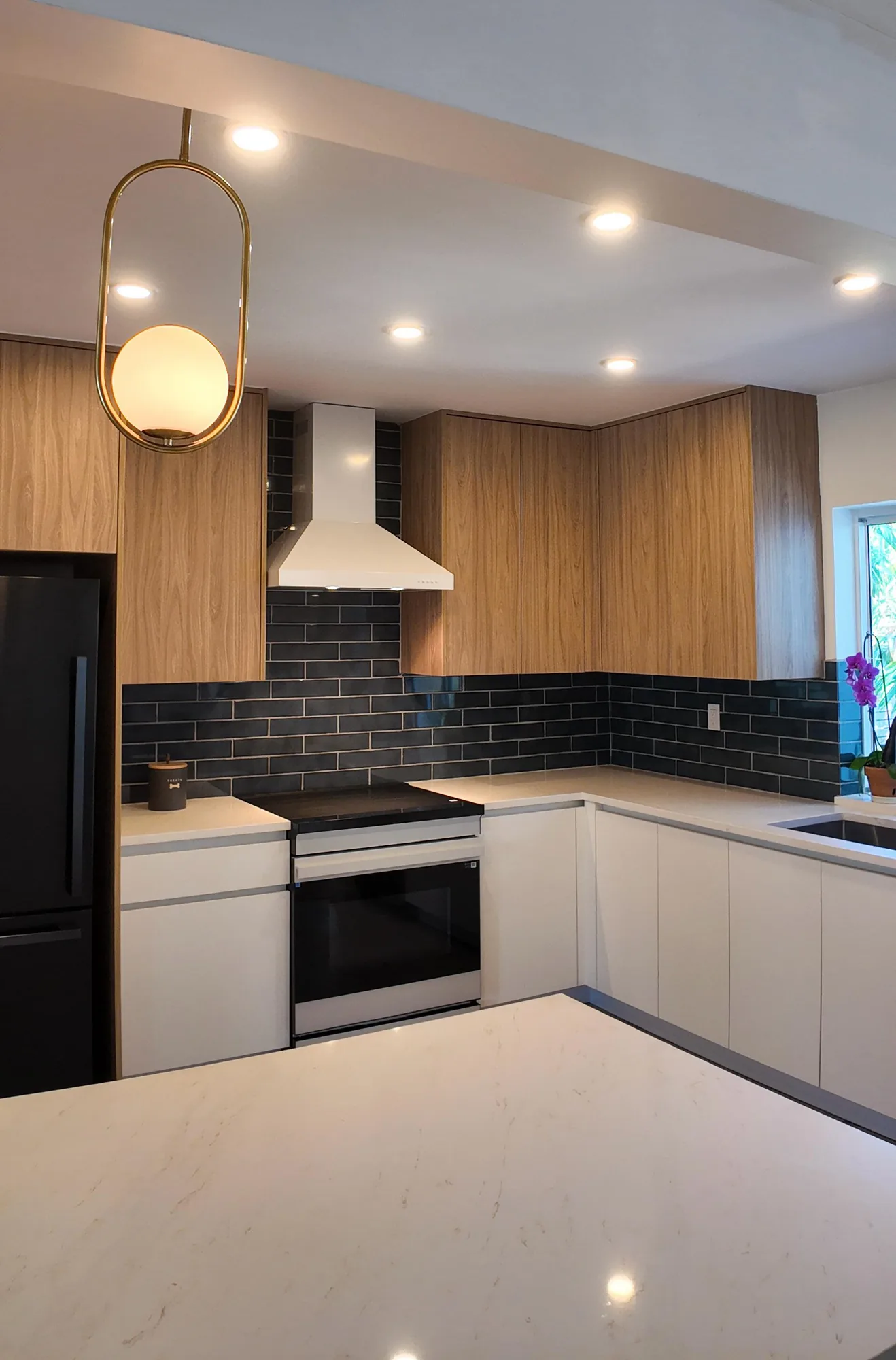 Light quartz counter in the foreground with wood cabinets, white lowers and a chimney hood beyond.