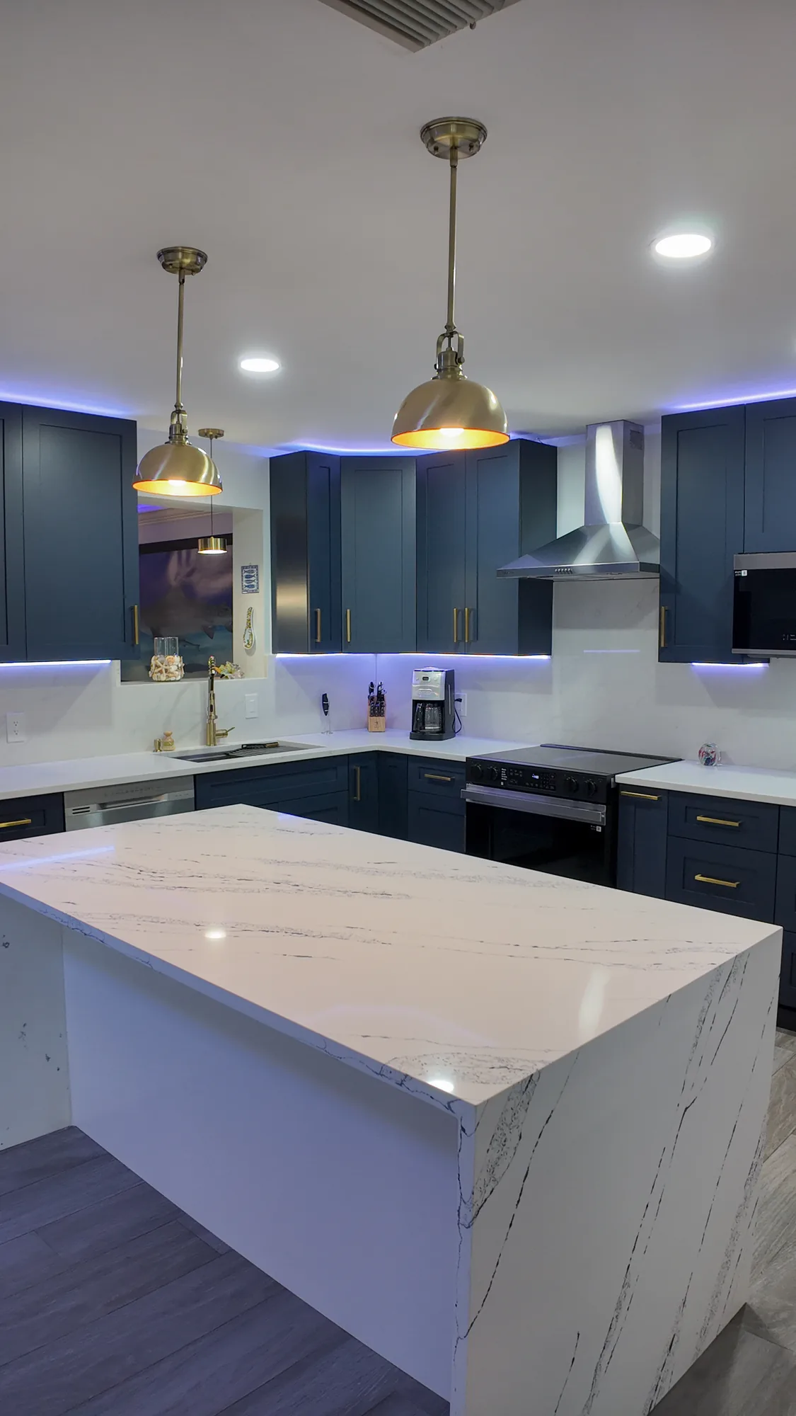 Close view of the white quartz island top with brass pendants above and LED cove lighting on the cabinets.