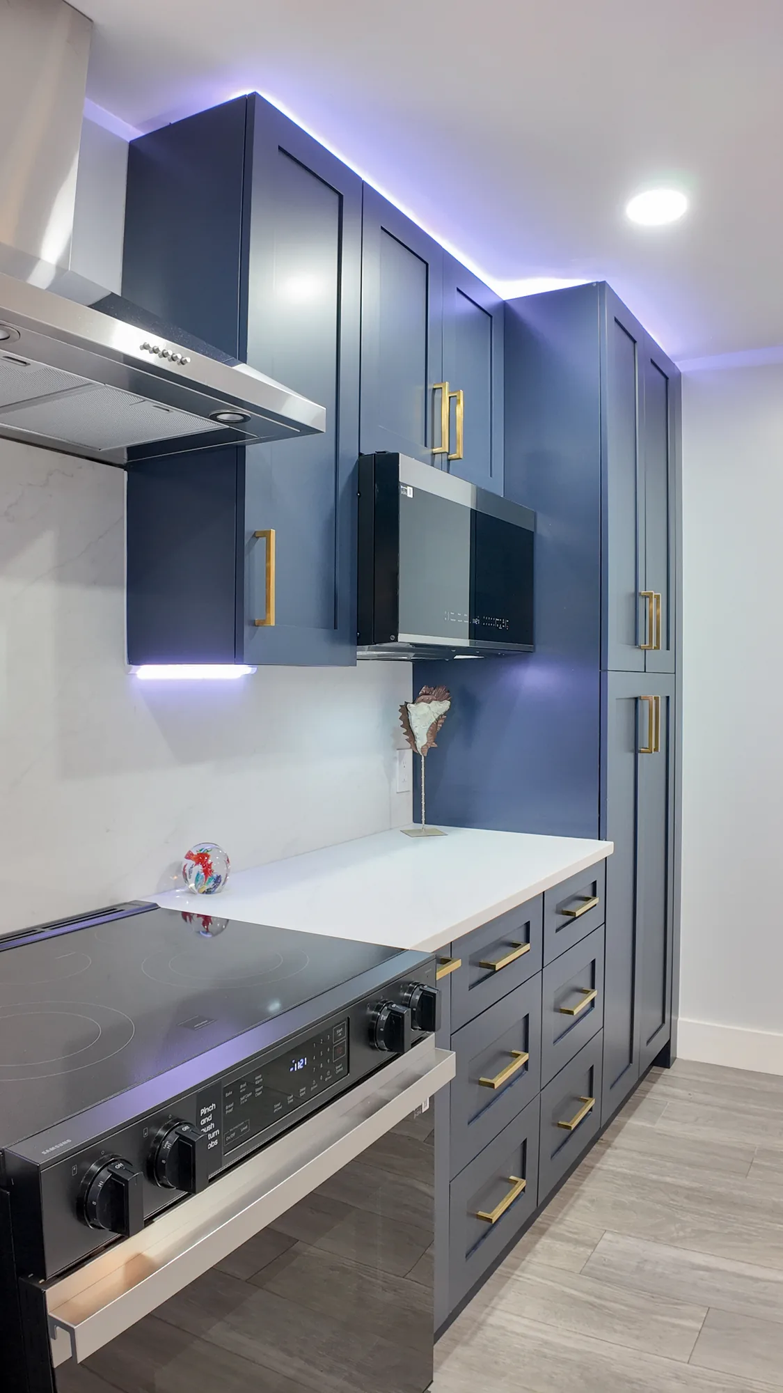 Stainless cooktop and hood beside a wall microwave, deep drawers and a tall navy pantry cabinet.