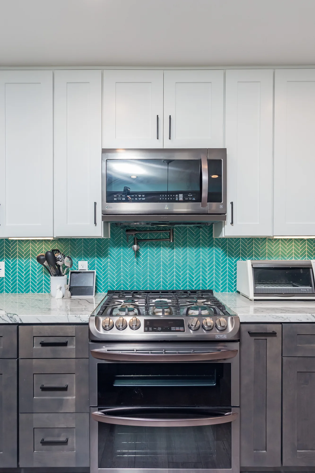 Range wall with white shaker cabinets, microwave, and teal tile running the full backsplash height.