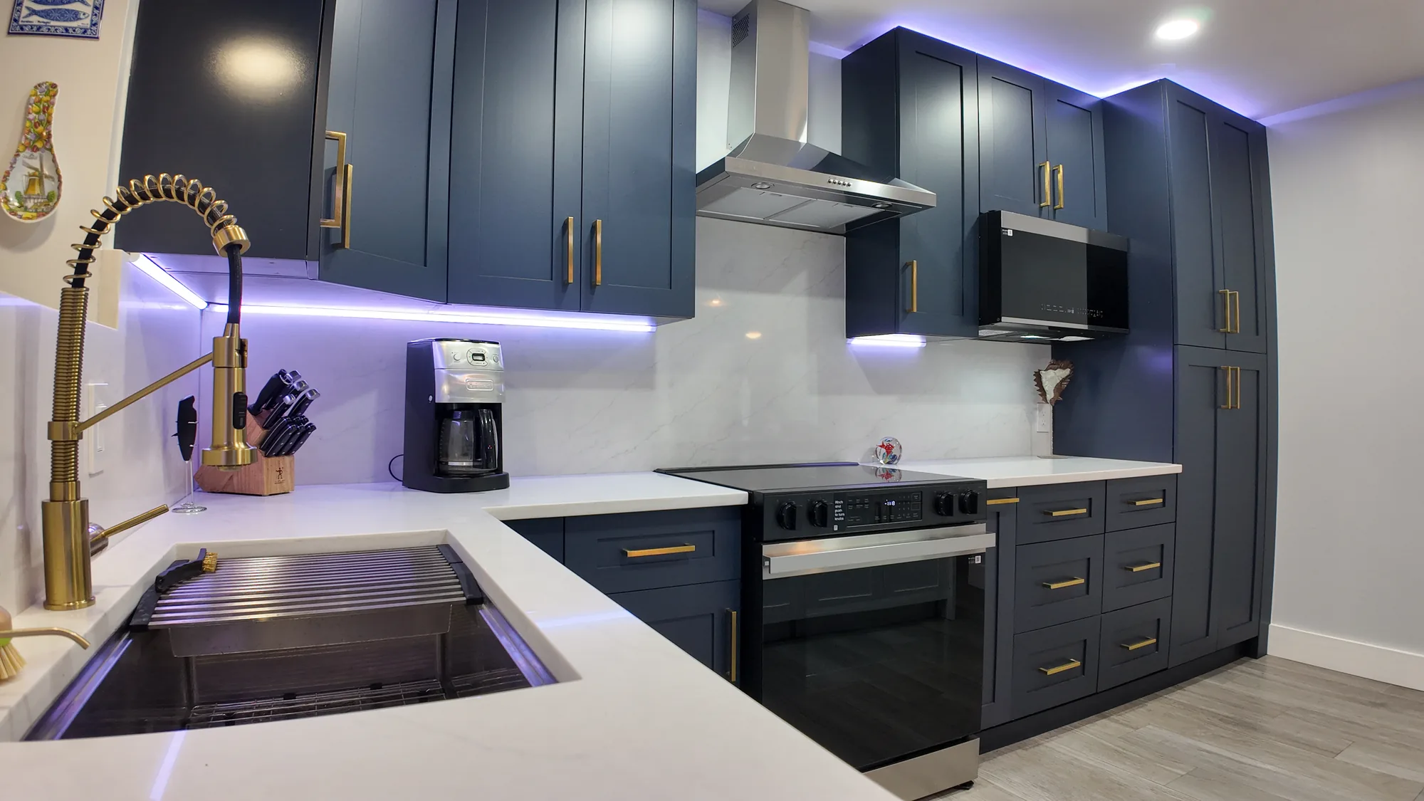 View across the sink toward a stainless range, chimney hood, wall microwave and floor-to-ceiling pantry.