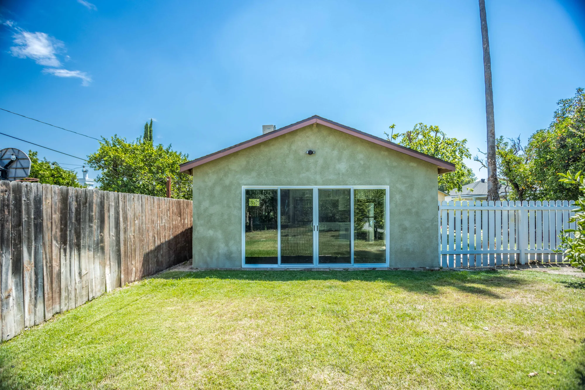 Rear elevation of a stucco addition with a gable roof and a wide sliding glass door facing the lawn.