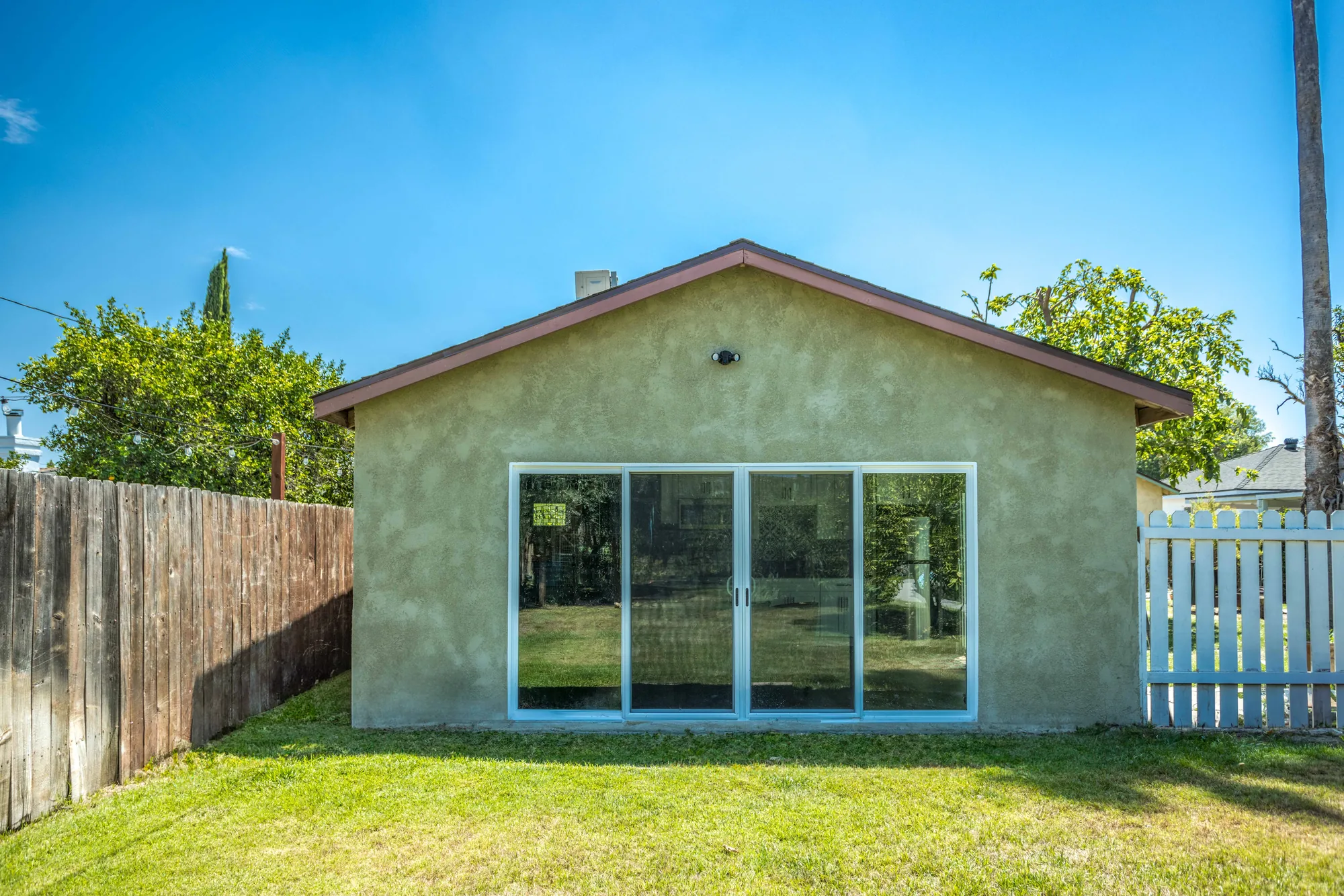 Straight-on view of the stucco gable wall with a wide sliding glass door and clear blue sky above.