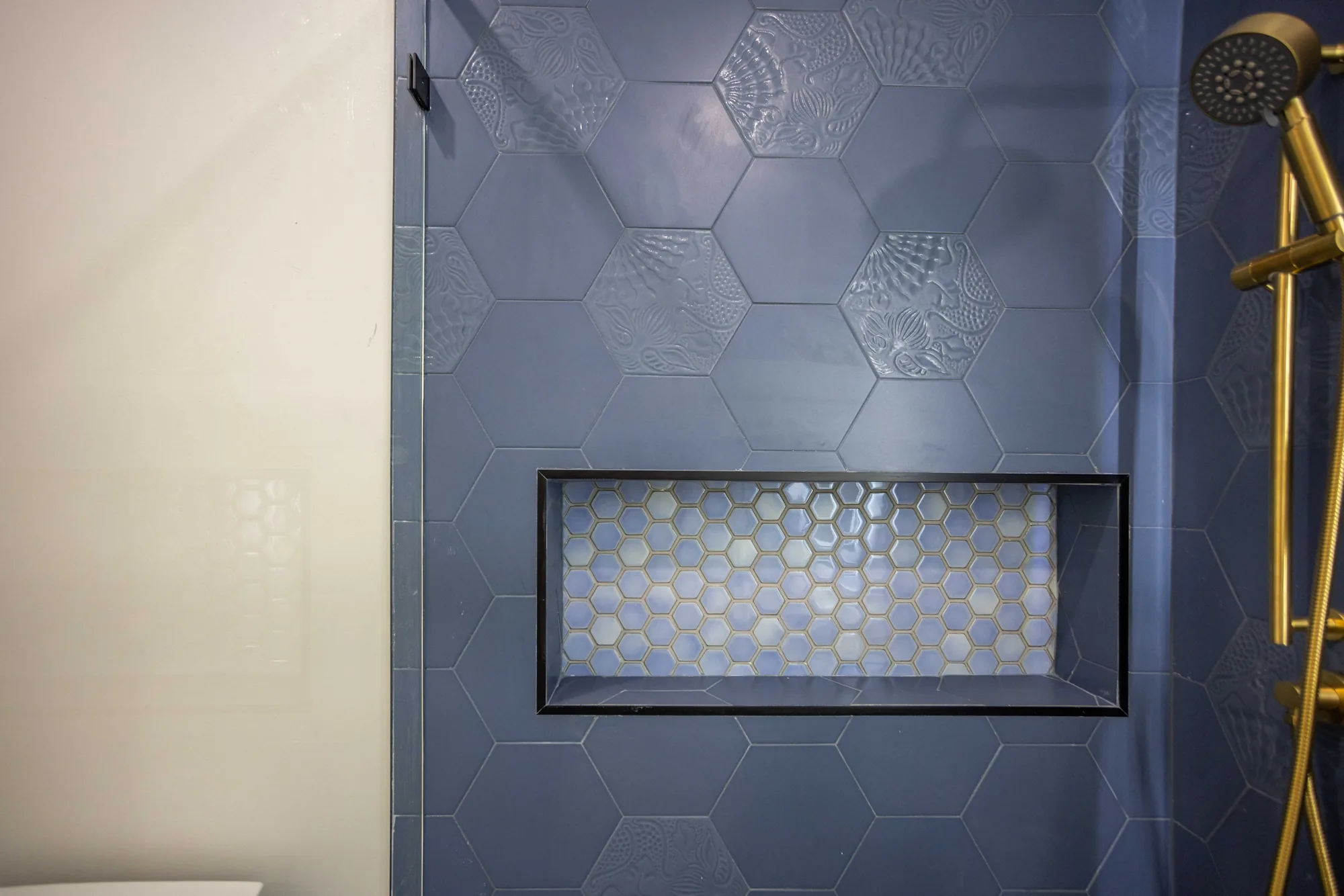 Recessed shower niche lined in pale hexagon mosaic and framed in black metal on navy tile.