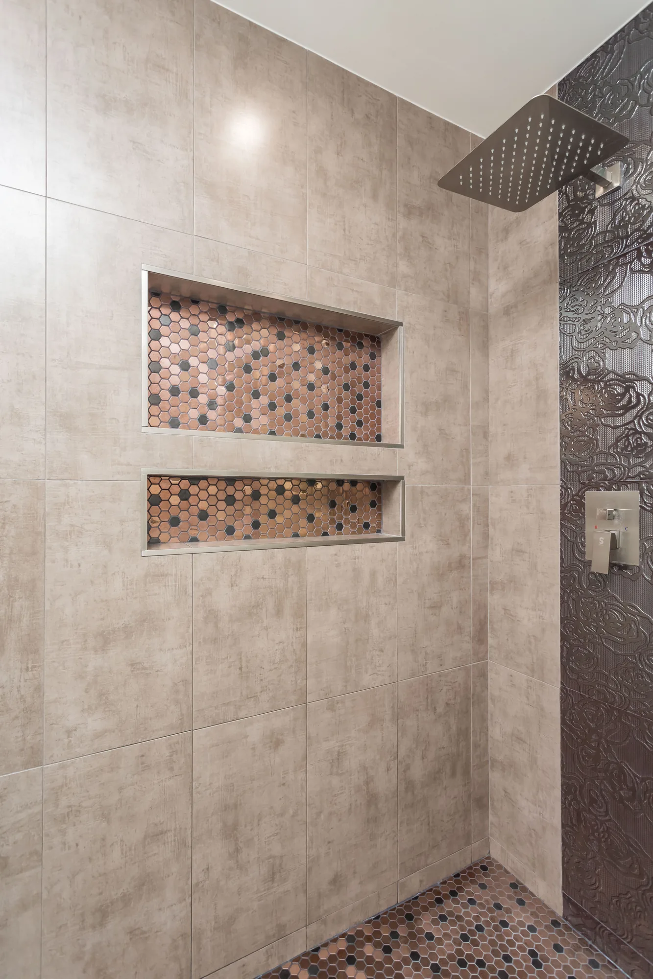 Two recessed shower niches lined with copper-tone hex mosaic beside a rain shower head.