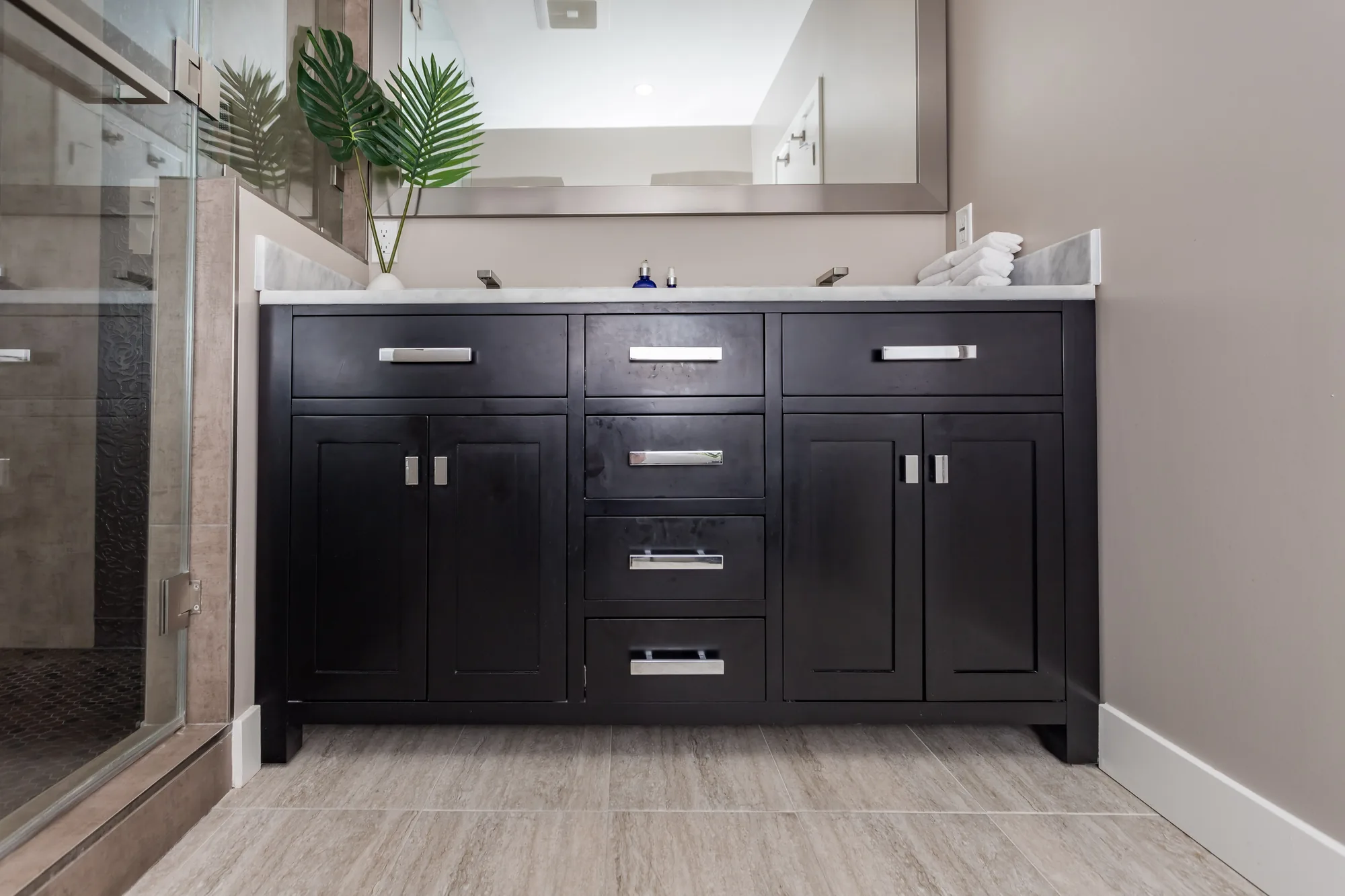 Close view of a dark shaker double vanity with brushed nickel pulls on tile flooring.