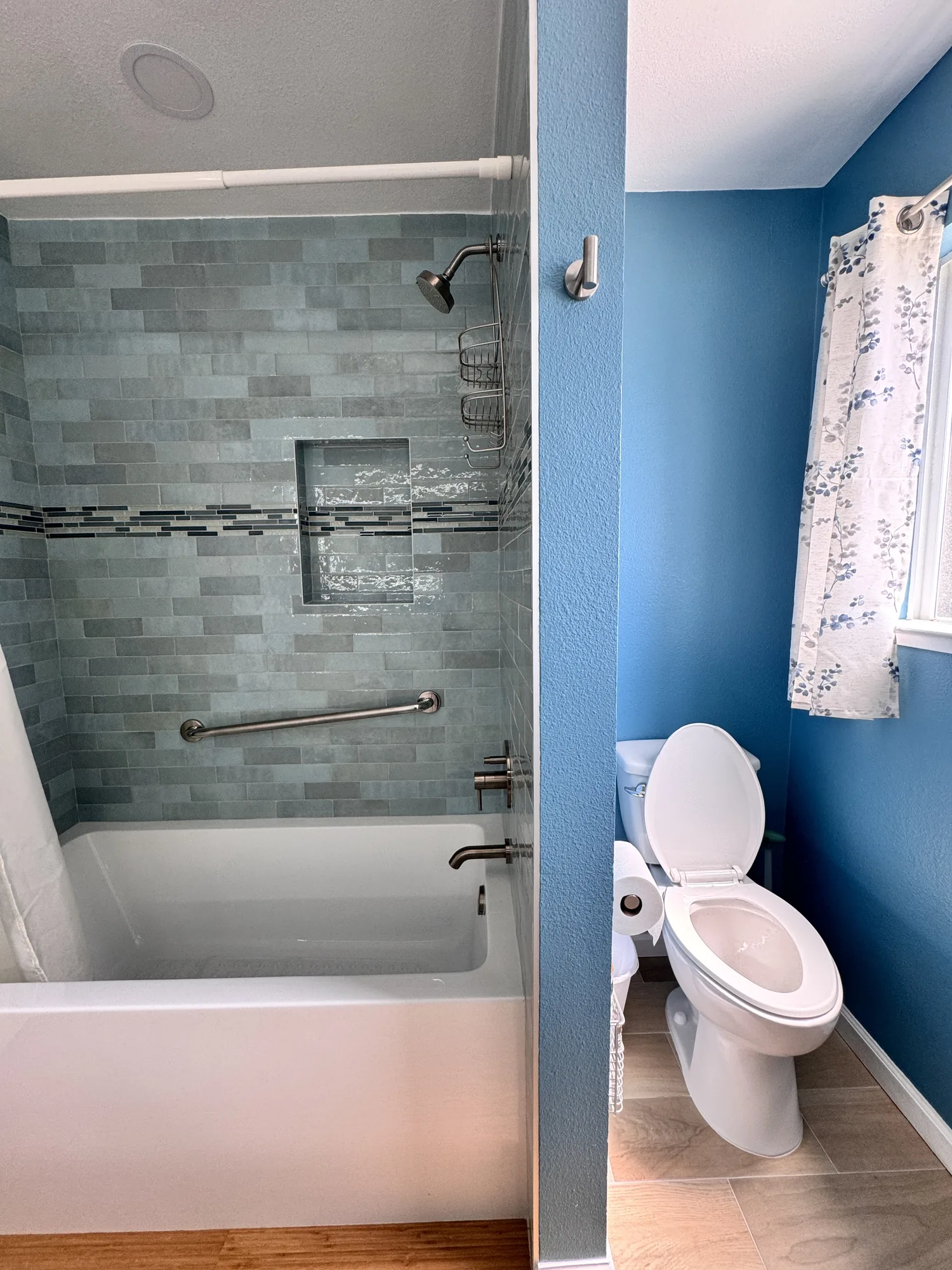 Tiled tub and shower on one side of a partition wall and the toilet alcove on the other.