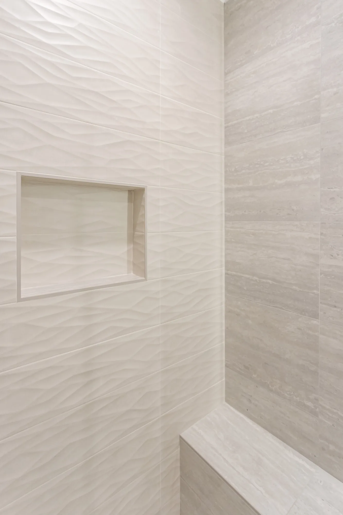 Shower corner detail showing a tiled niche, wavy accent tile and a built-in stone-look bench seat.