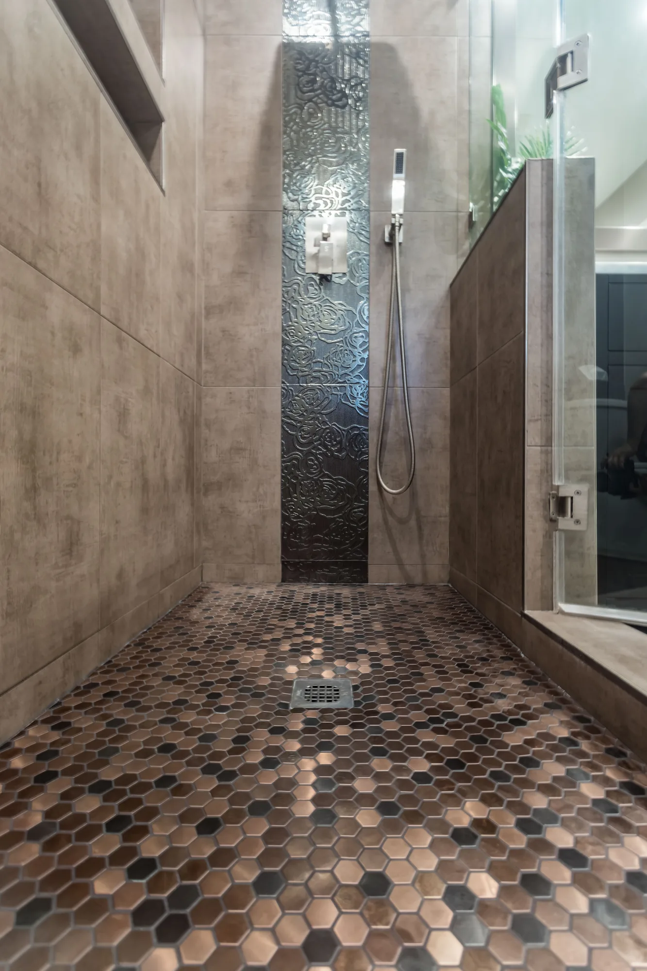 Walk-in shower floor in copper-tone hex mosaic with a square center drain and glass panel.