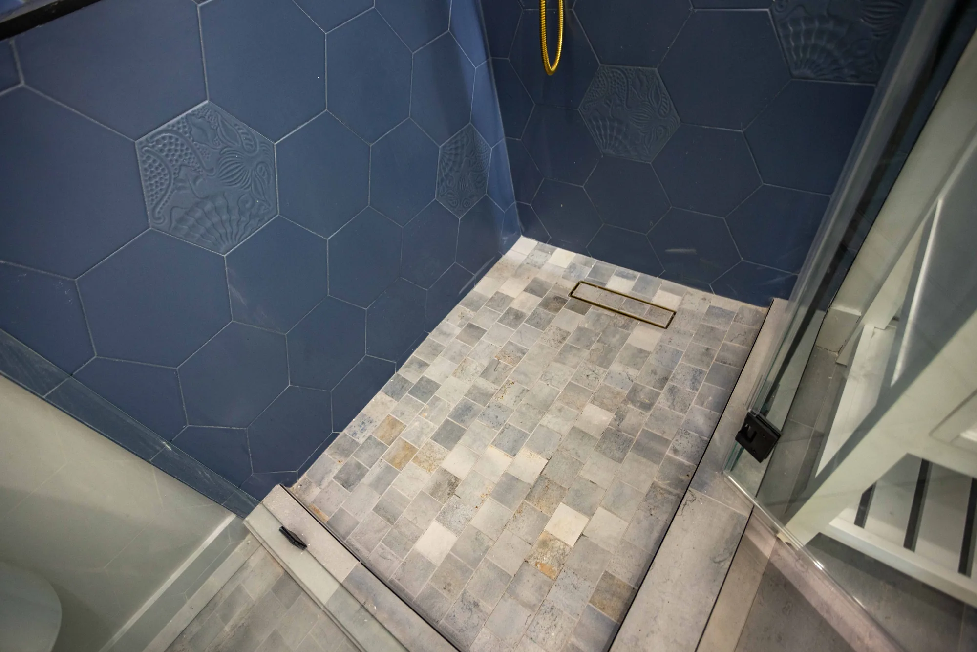 Looking down at a mosaic shower floor with a linear drain, low curb and navy tiled walls.