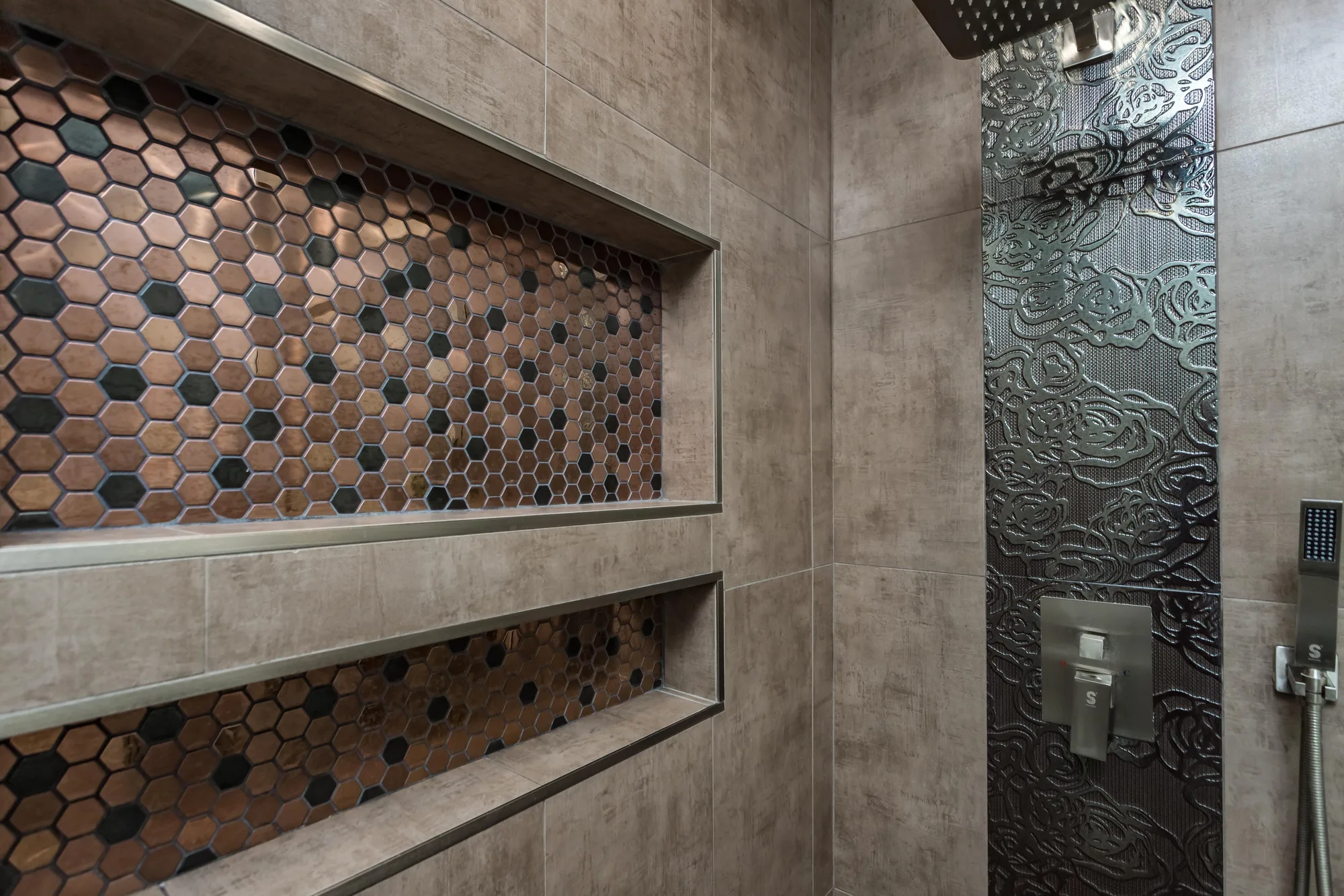 Close view of metal-trimmed shower niches in hex mosaic beside embossed dark accent tile.