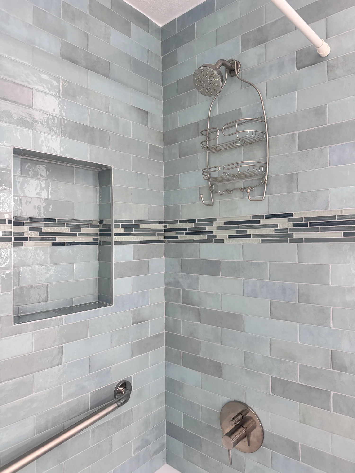 Tiled shower corner with a recessed niche, brushed nickel showerhead and single handle valve trim.
