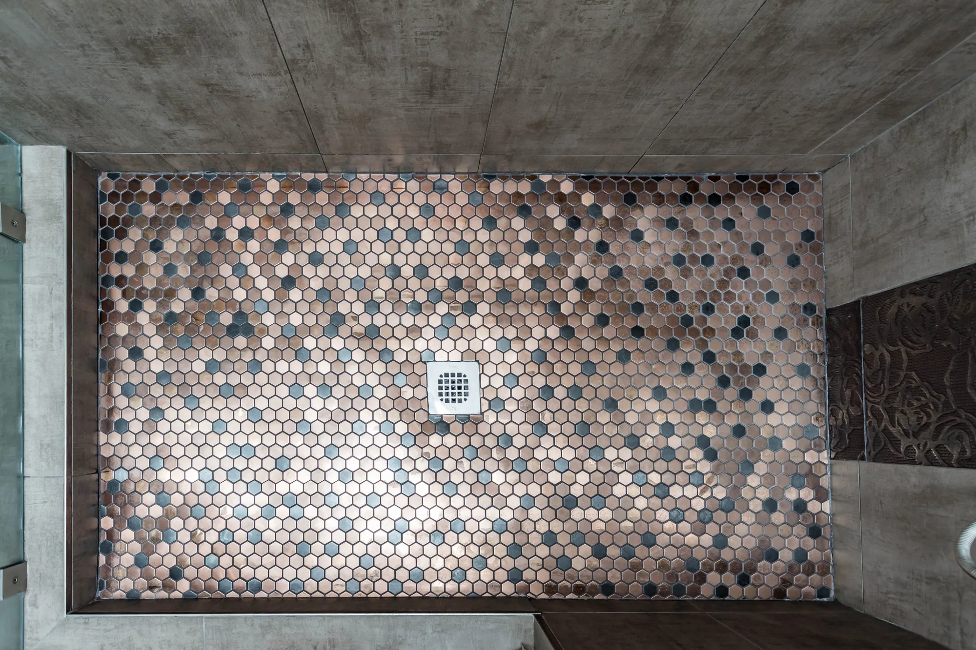 Top-down view of a walk-in shower pan tiled in copper and grey hexagon mosaic.