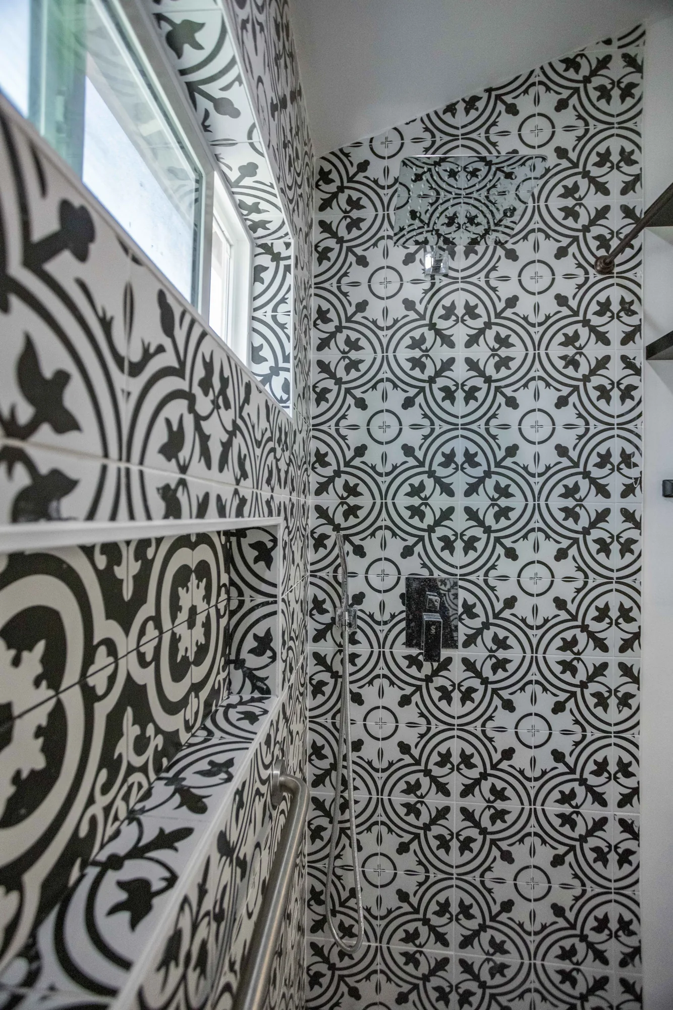 Close view of black and white patterned shower tile wrapping the corner beside a small window.