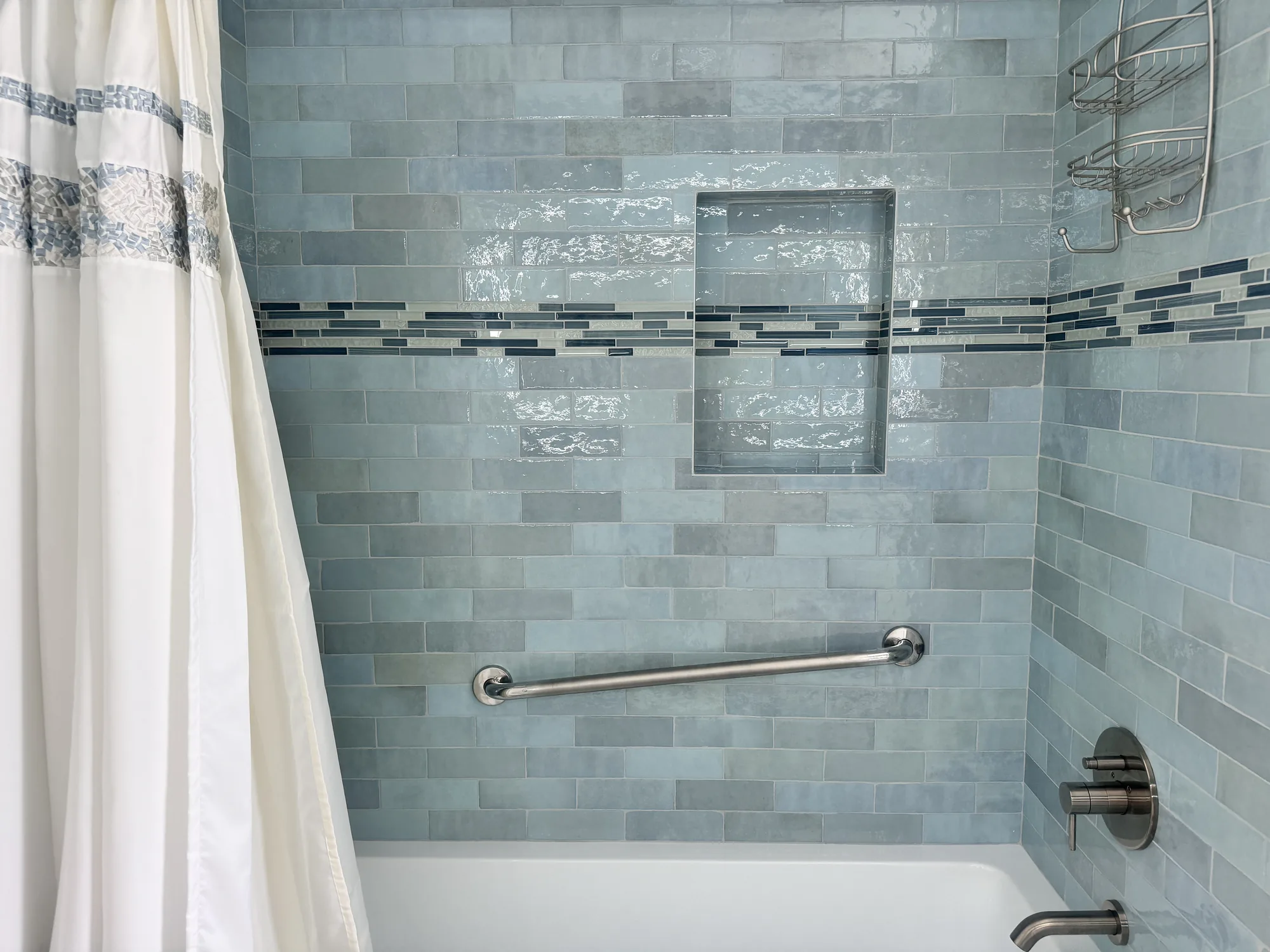 Close view of blue-green tile shower wall where a mosaic stripe runs through a recessed niche.