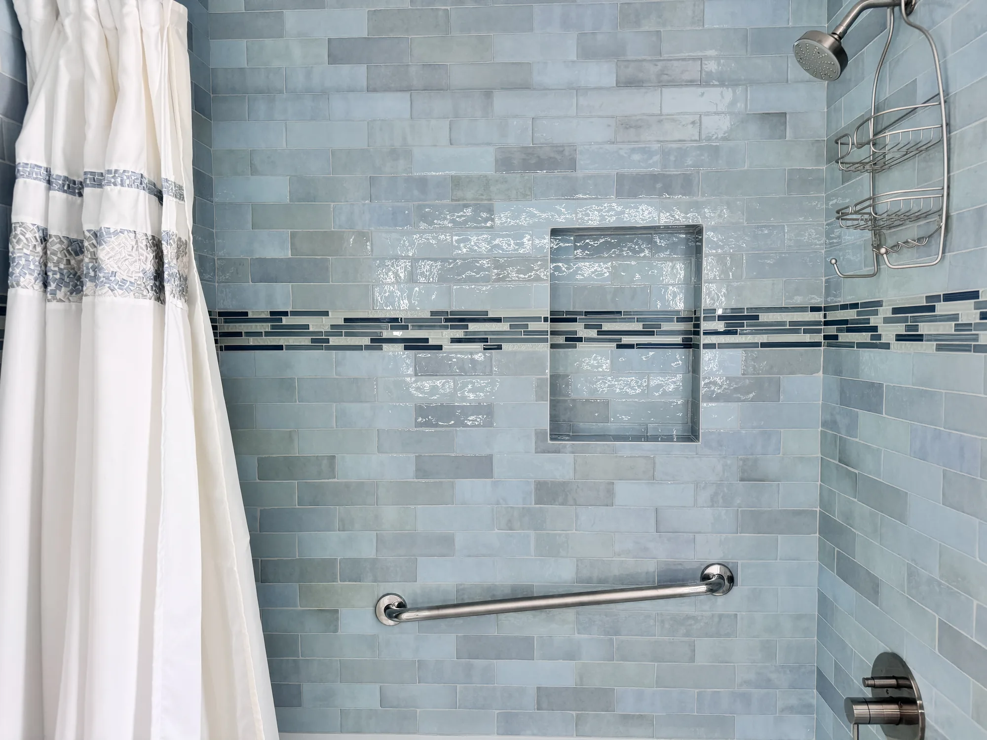Blue-green tiled shower wall with a recessed niche, brushed nickel showerhead and grab bar.